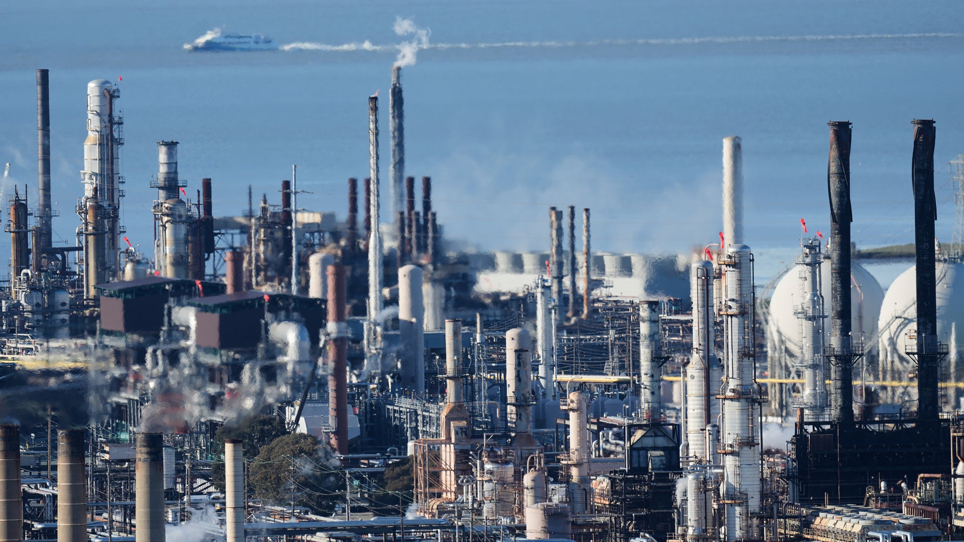 Industriell raffinaderi med många höga skorstenar och processingkonstruktioner mot blå himmel