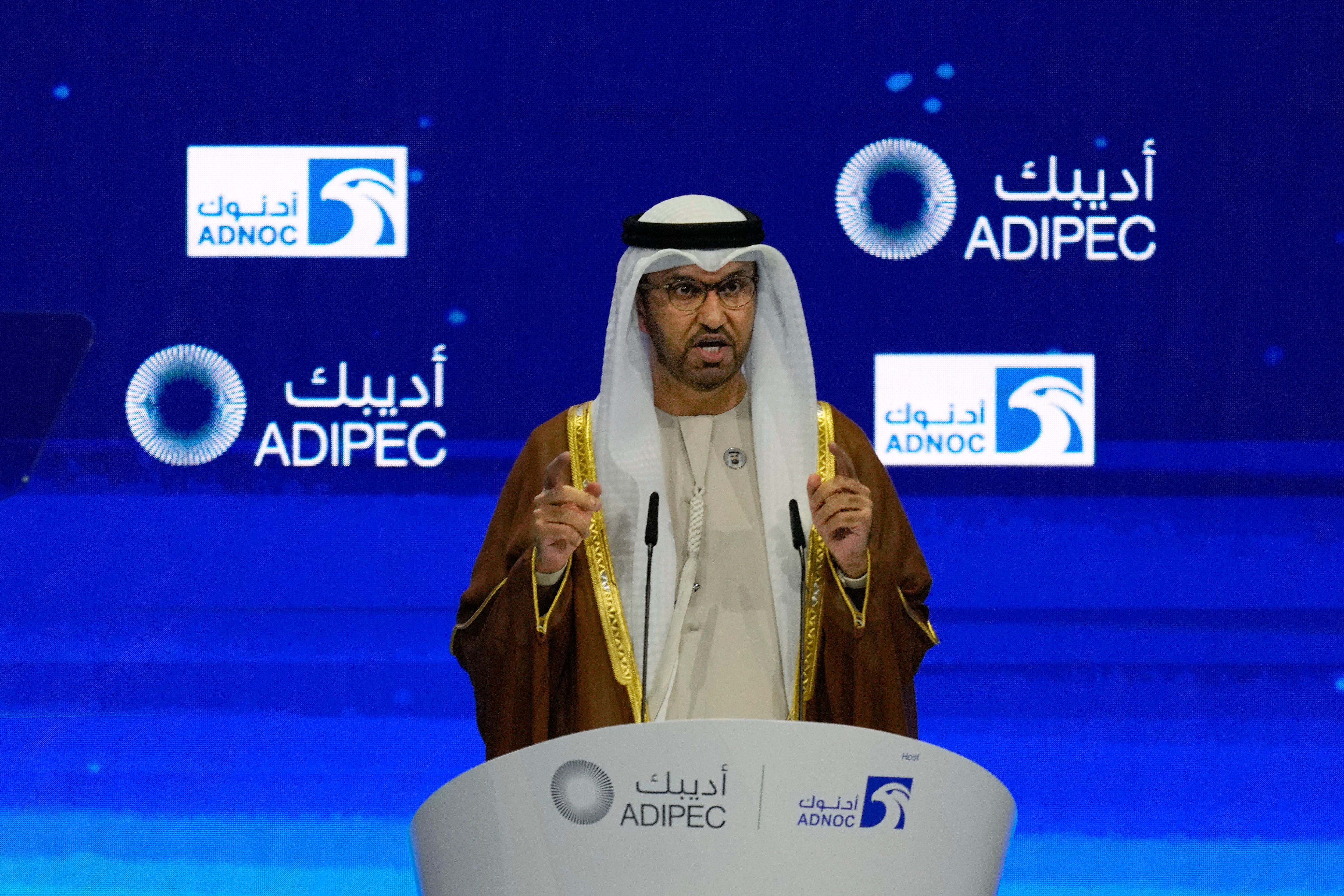 Man i traditionell arabisk klädedräkt talar vid ett podium med ADNOC och ADIPEC logotyper i bakgrunden.