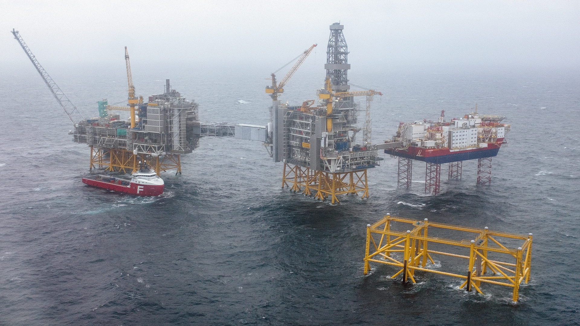 Flera oljeplattformar och båtar på öppet hav under dimmiga väderförhållanden.