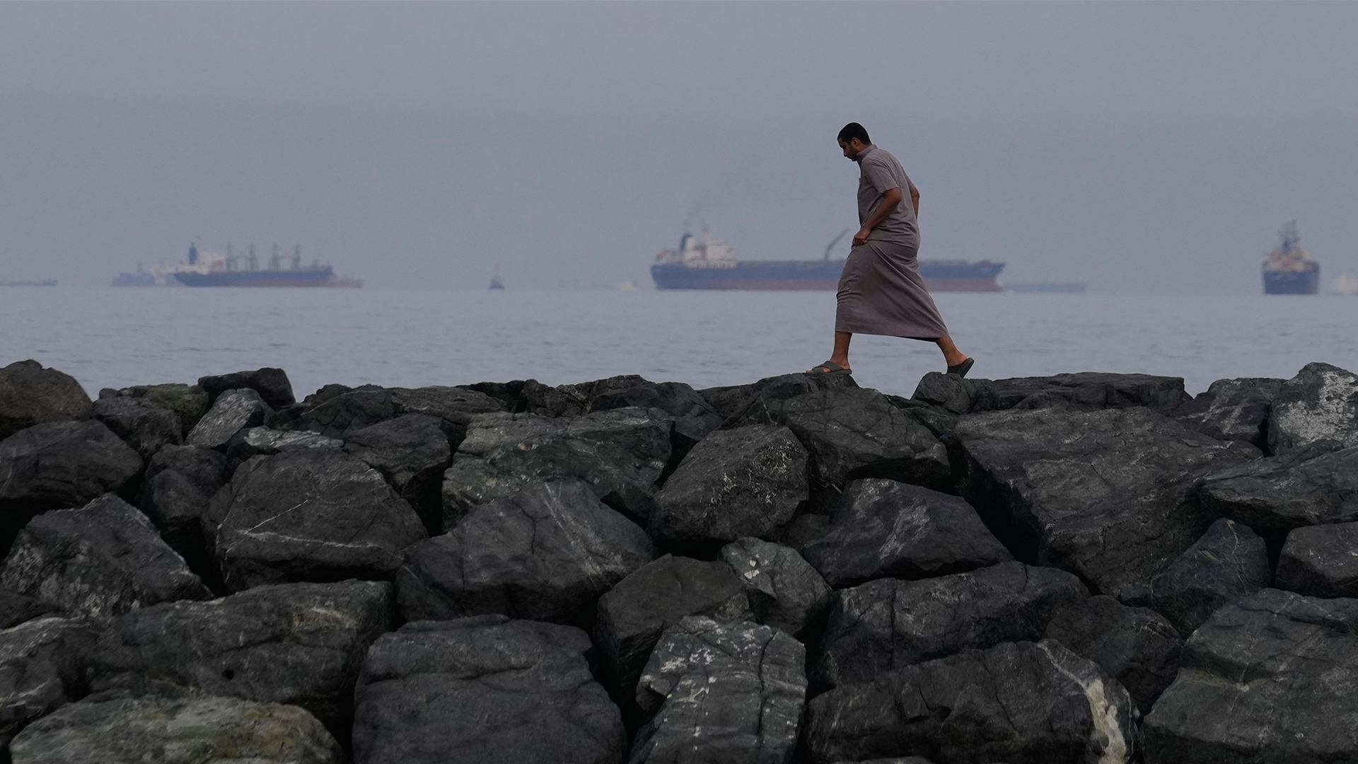Person går på stora stenar längs Hormuzsundet. Fartyg syns i bakgrunden.