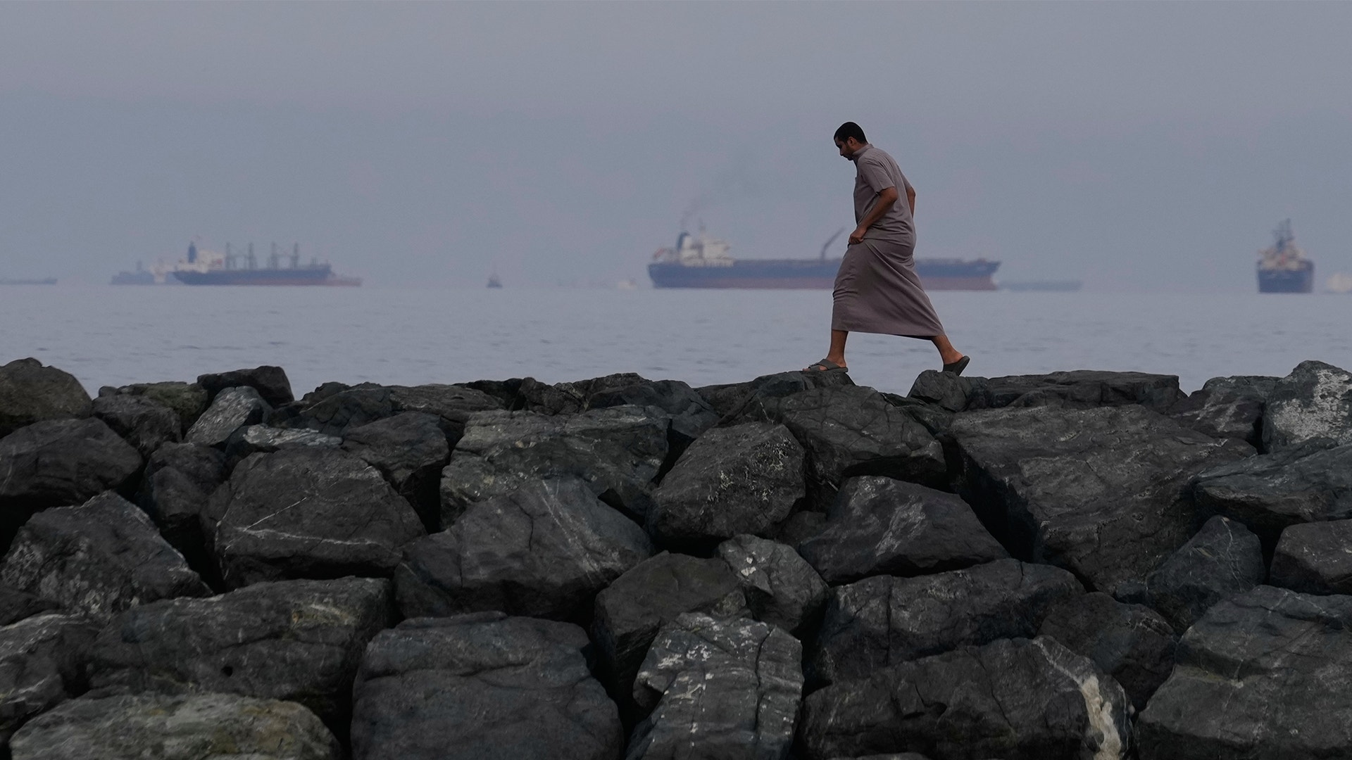 Person går på stora stenar längs Hormuzsundet. Fartyg syns i bakgrunden.