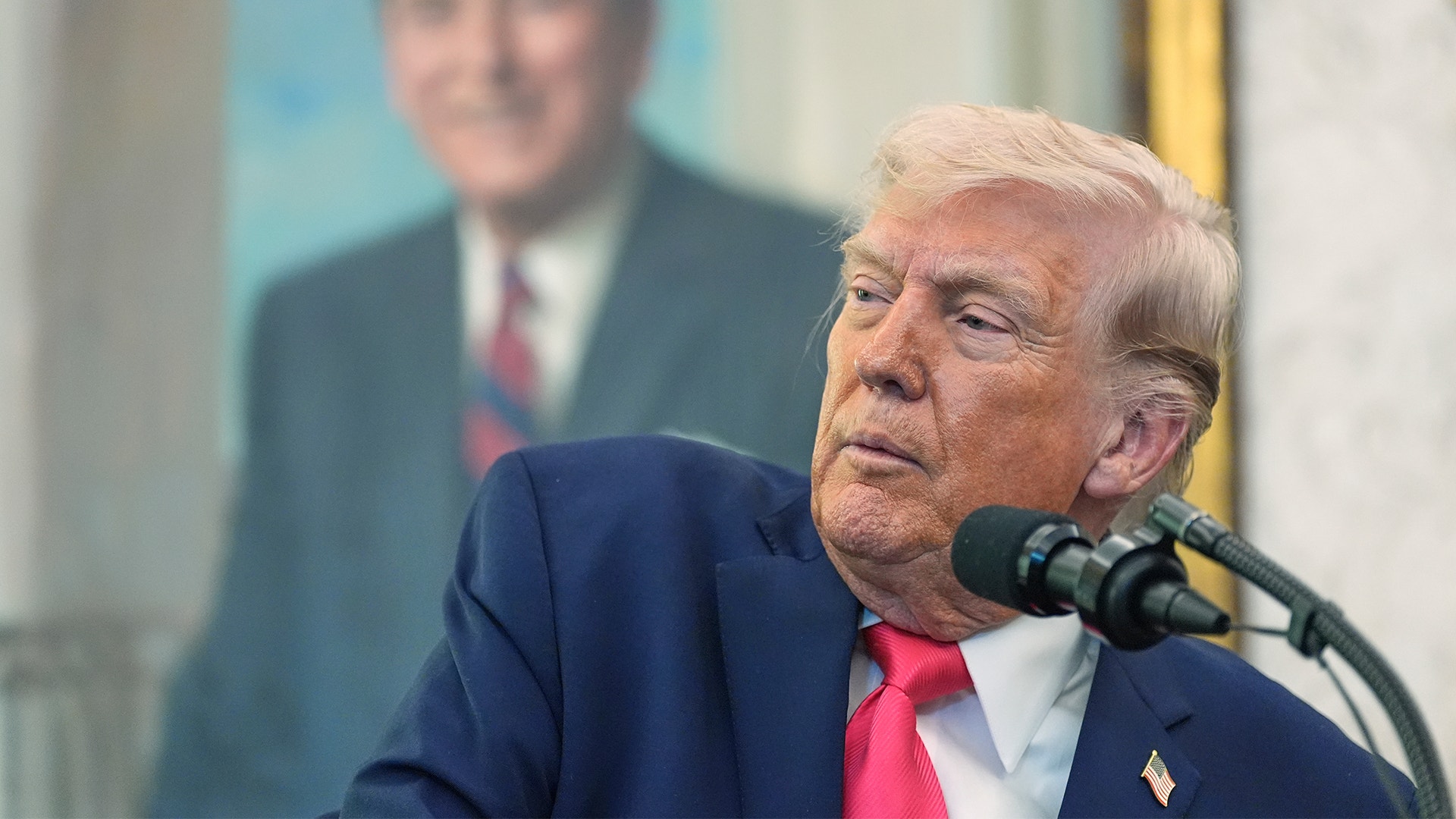 En man i mörkblå kostym och röd slips talar vid en mikrofon.