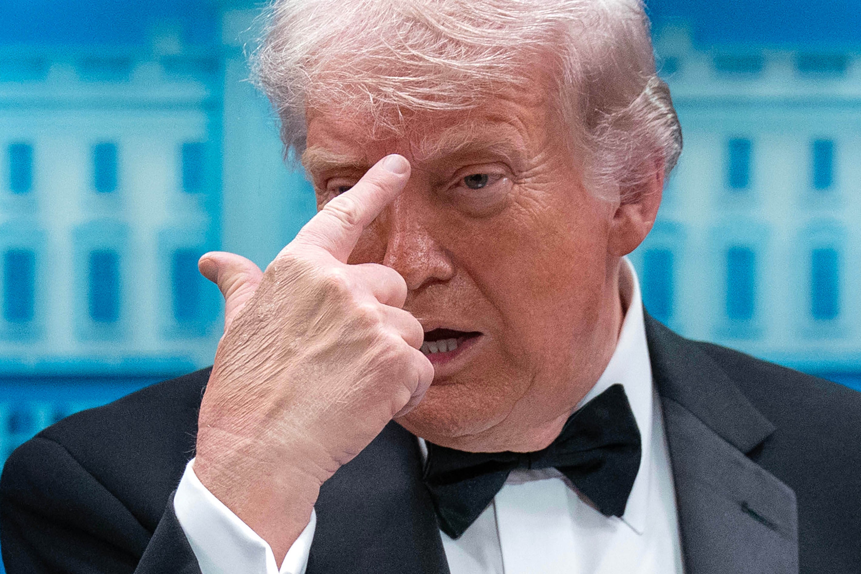 Man i smoking som pekar med fingret mot kameran framför en blå byggnad.