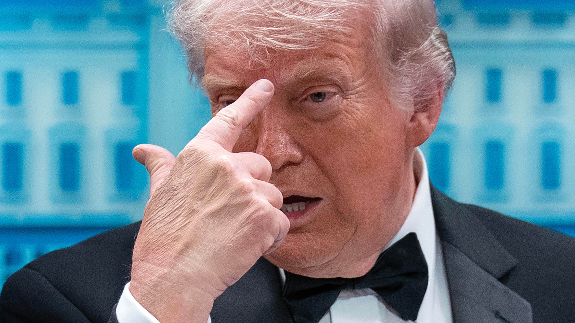 Man i smoking som pekar med fingret mot kameran framför en blå byggnad.