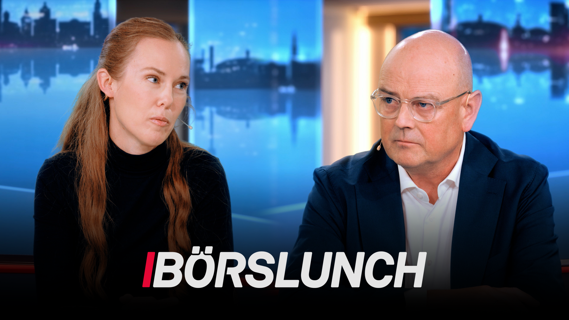 Två personer i TV-studio för finansprogrammet Börslunch. En kvinna och en man sitter vid studiobord med stadshorisont i bakgrunden.