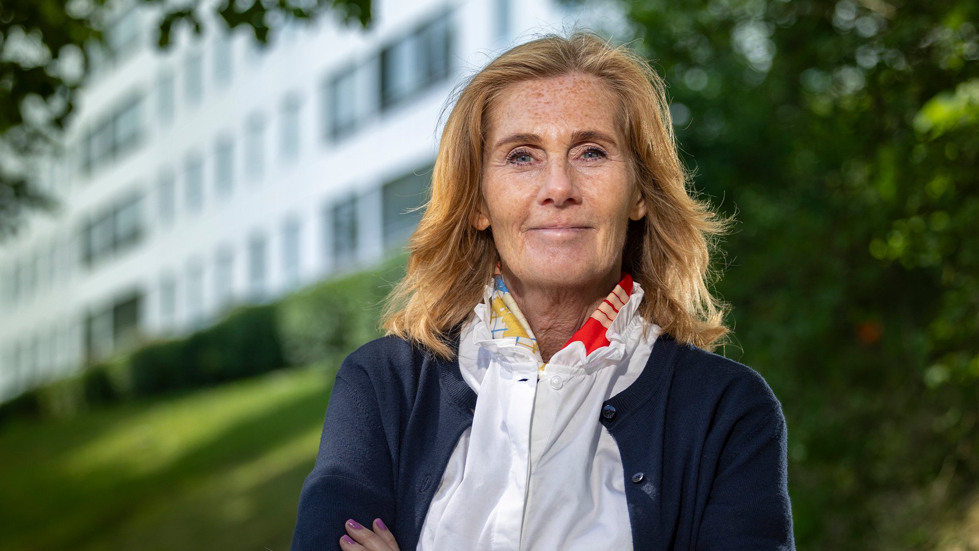 Anette Frumerie står med händerna i kors framför ett av Rikshems fastigheter i ett blommande juni.