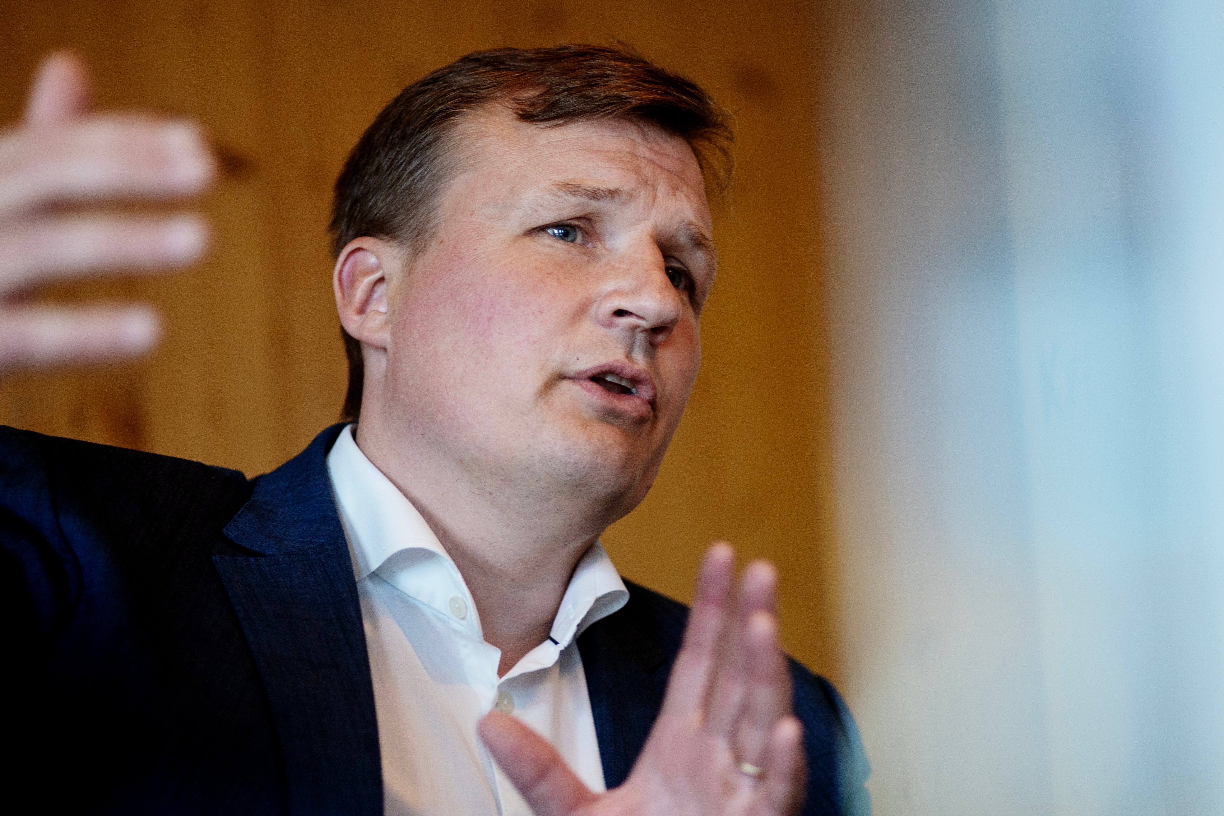 Man i mörk kostym och ljus skjorta som gestikulerar och talar.