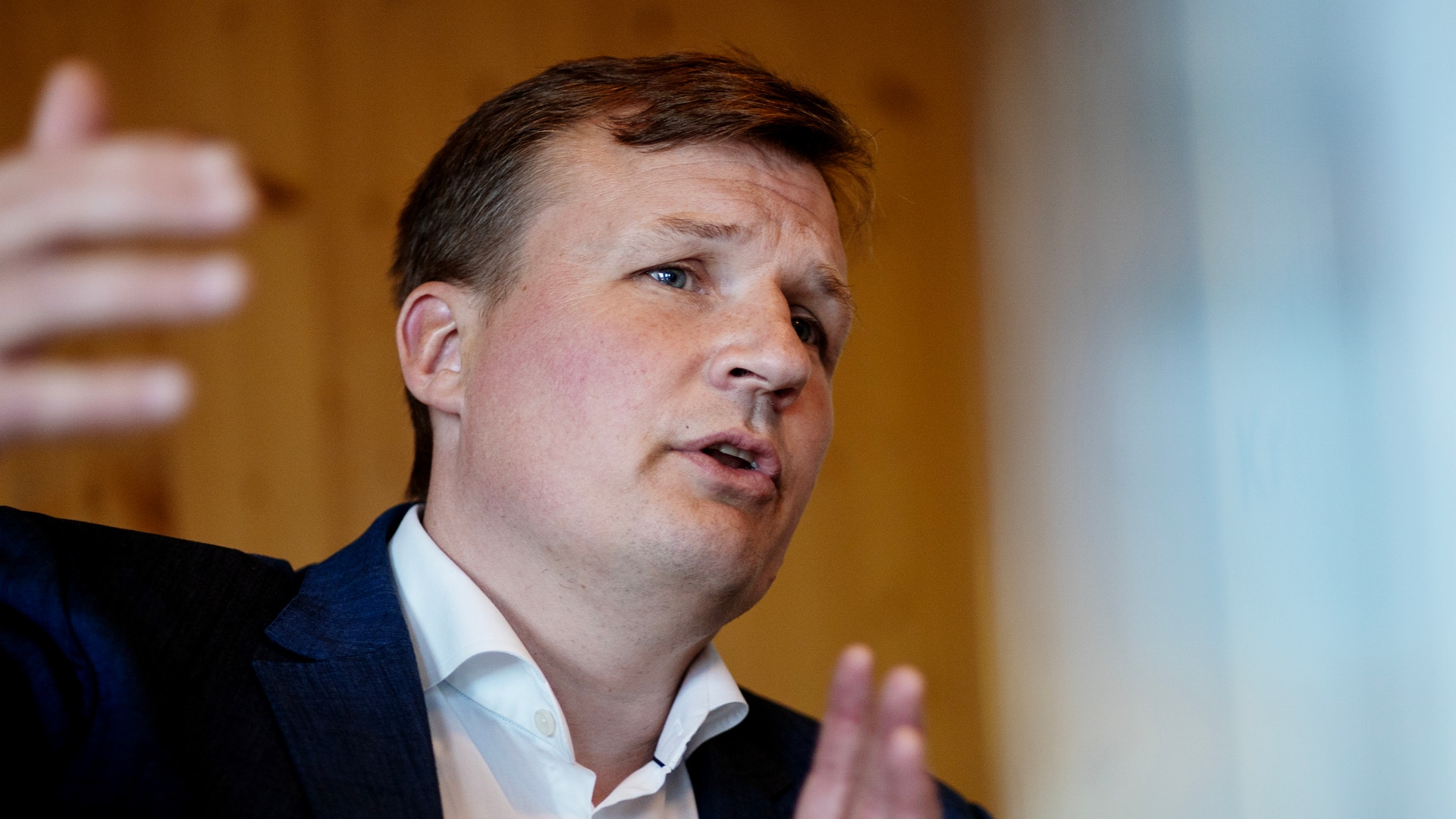 Man i mörk kostym och ljus skjorta som gestikulerar och talar.