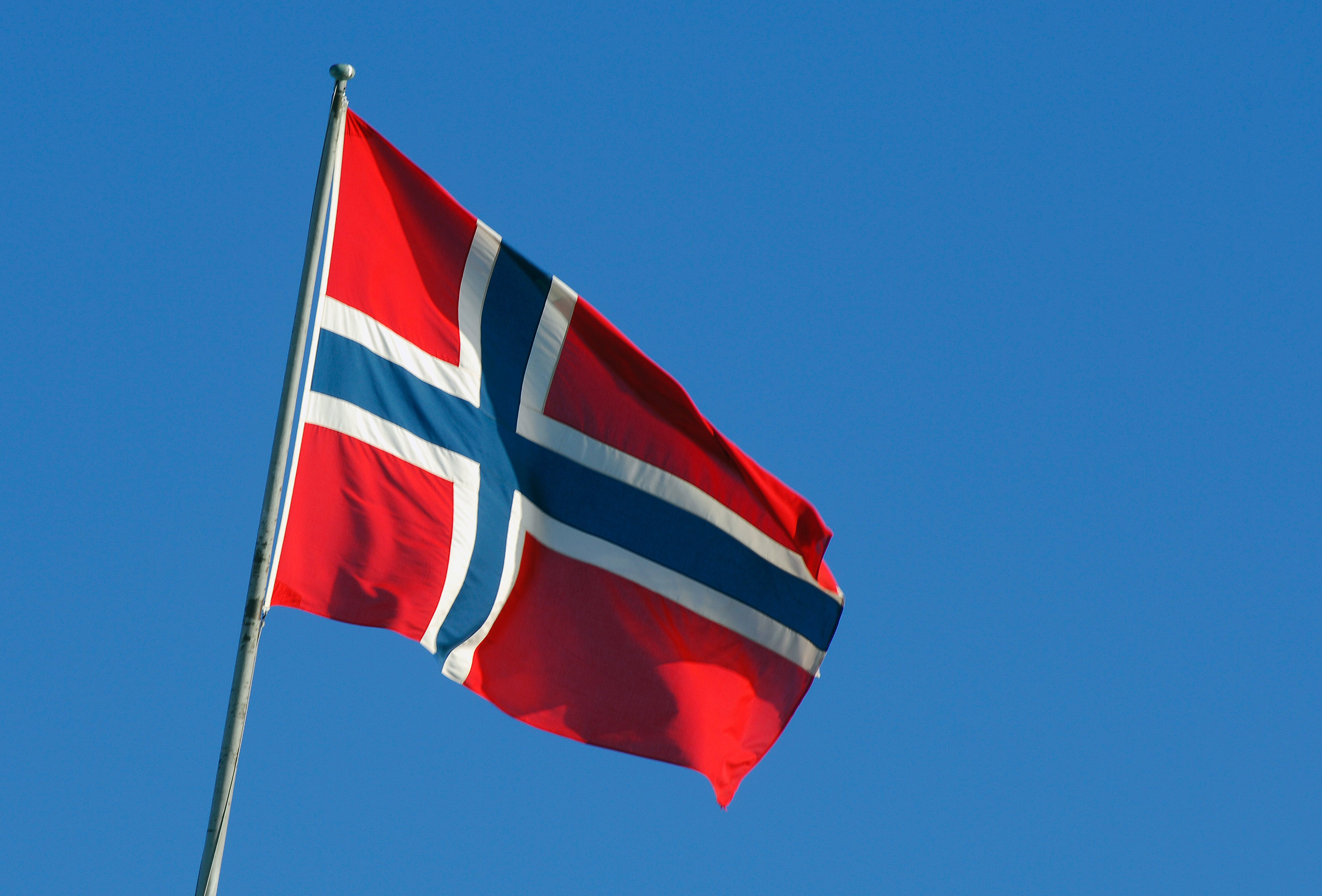 Norges flagga som vajar på en flaggstång mot en klarblå himmel.