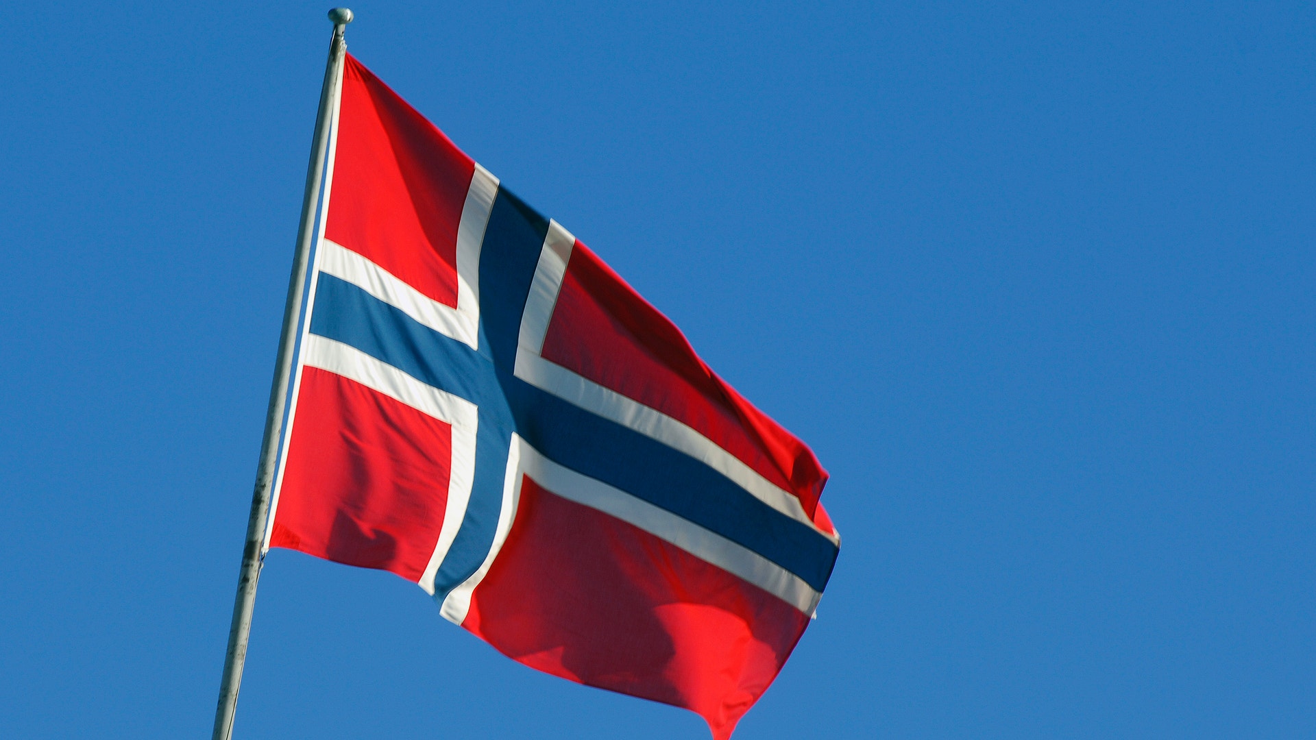 Norges flagga som vajar på en flaggstång mot en klarblå himmel.