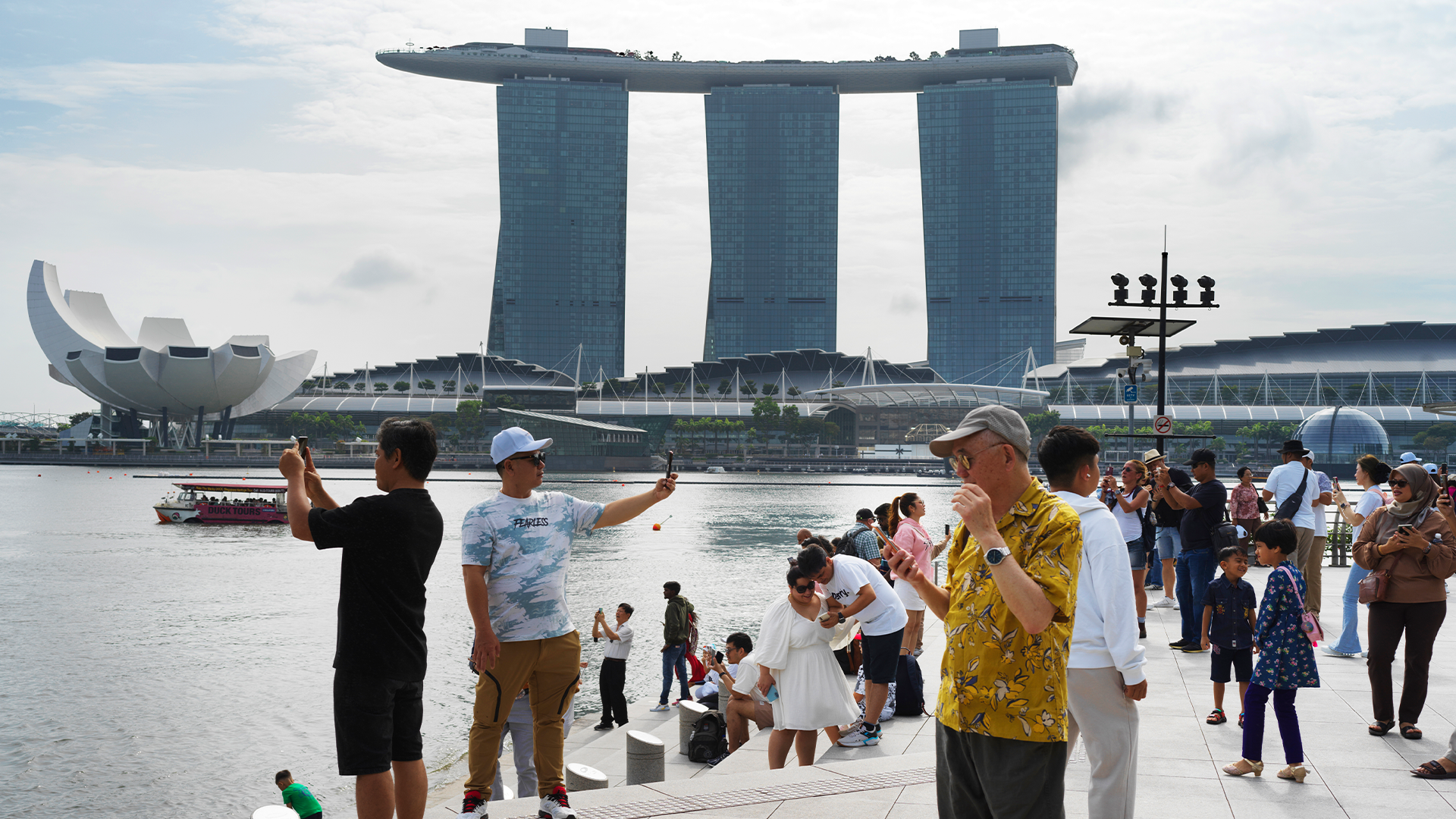 Personer tar bilder vid floden i Singapore. Det är fint väder. 