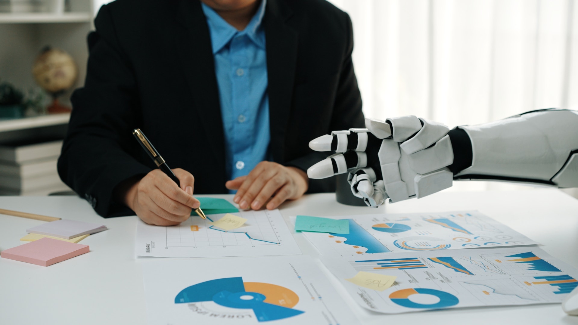 Person med robotarm arbetar vid skrivbord med diagram och affärsdokument