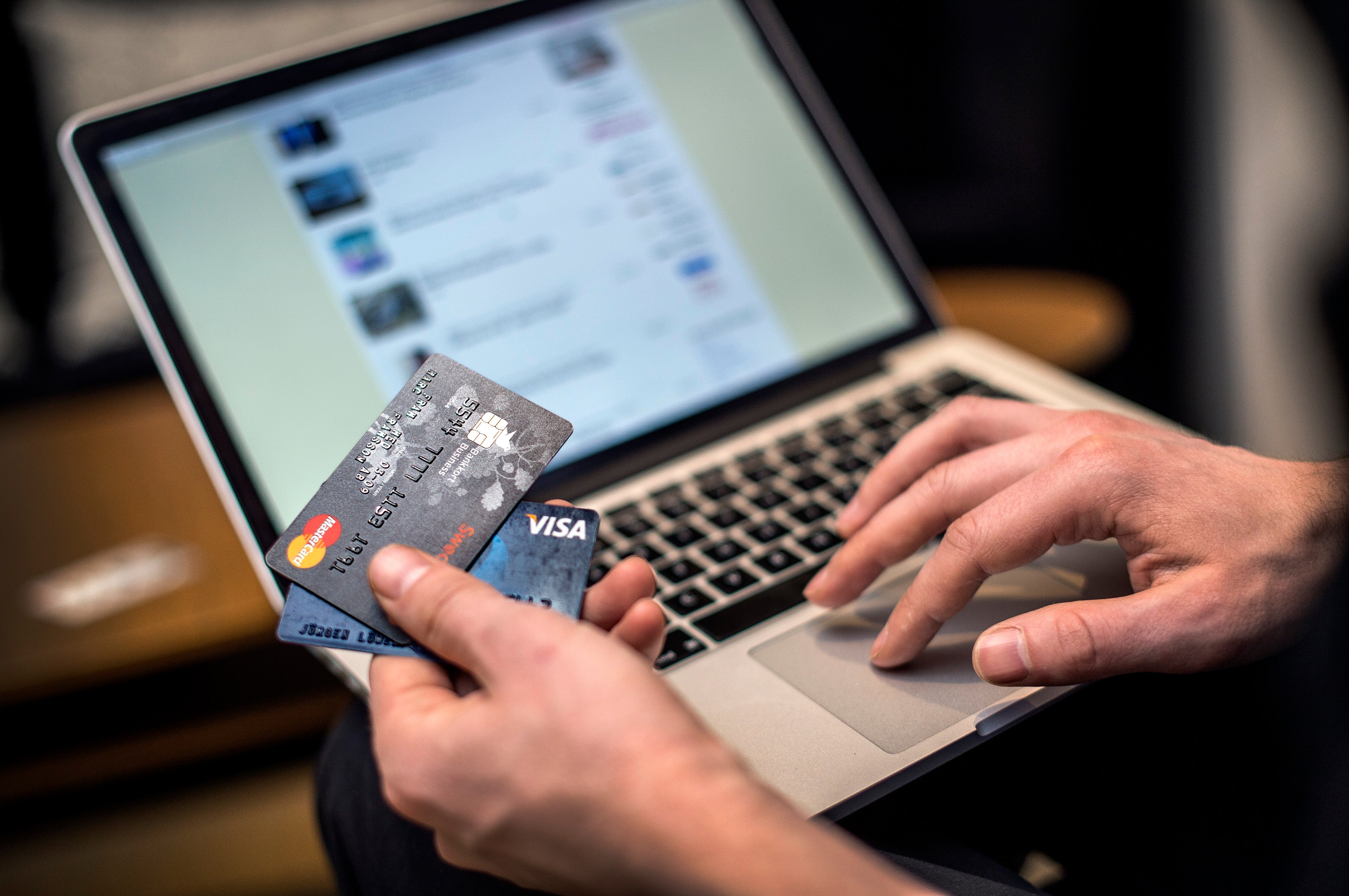 En person håller ett kreditkort framför en laptop-skärm som visar en webbutik eller betalningssida. Personens högerhand vilar på tangentbordet medan vänsterhand håller kortet. Bilden illustrerar online-shopping, e-handel och säker digital betalning.
