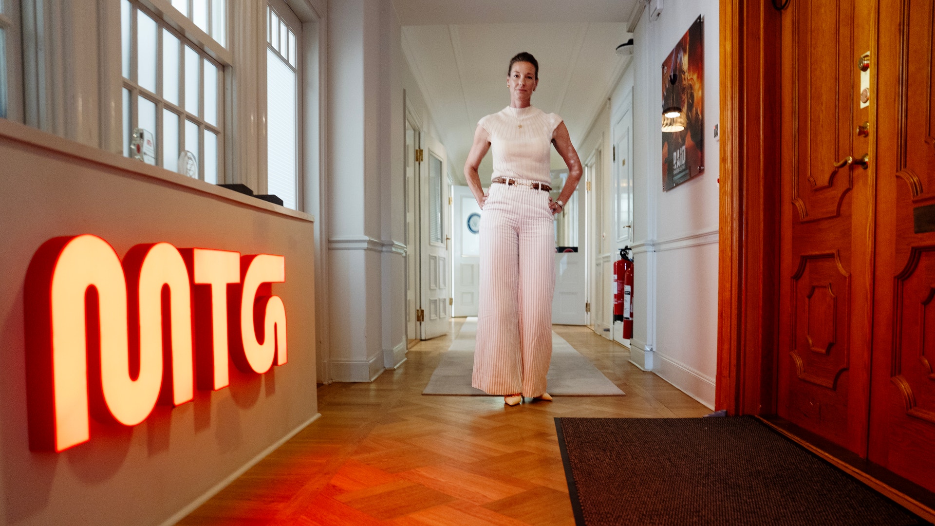 Kvinna i ljusa kläder står i en hallway med ett rött neonskylte bakom sig.