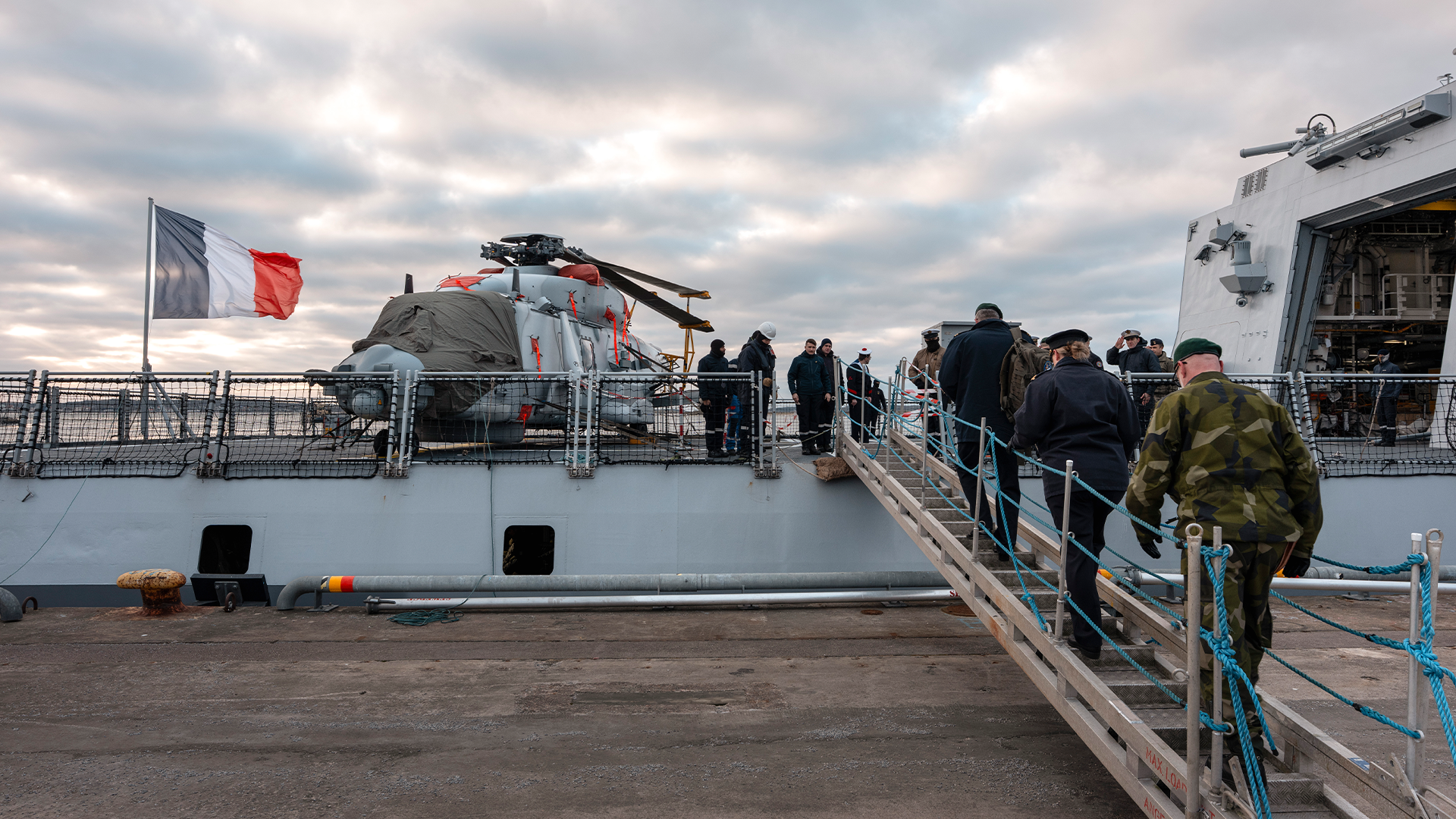 Militär fregatt med besökare som går ombord via en landgång. Franska flaggan är hissad på skeppet.