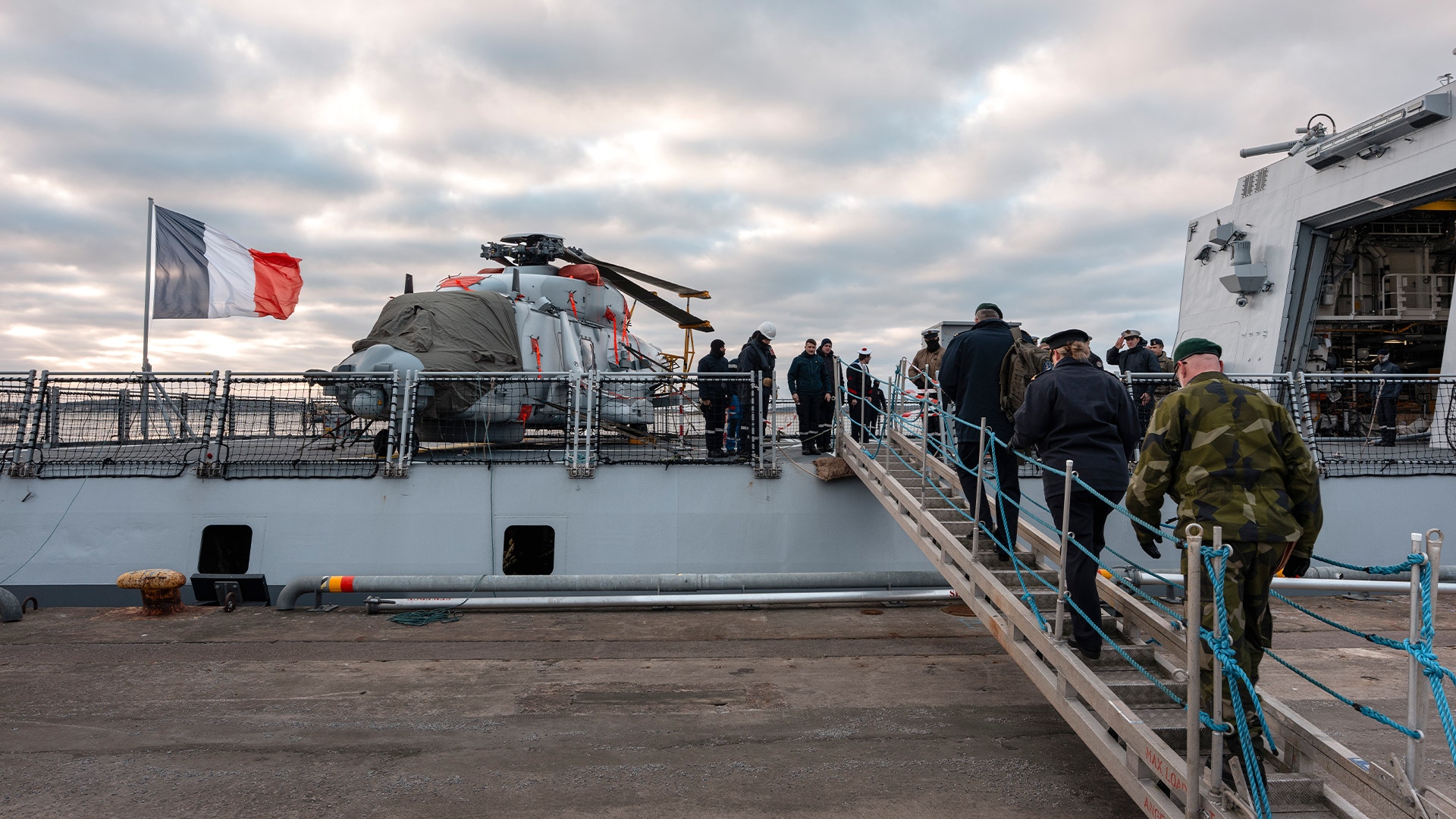 Militär fregatt med besökare som går ombord via en landgång. Franska flaggan är hissad på skeppet.