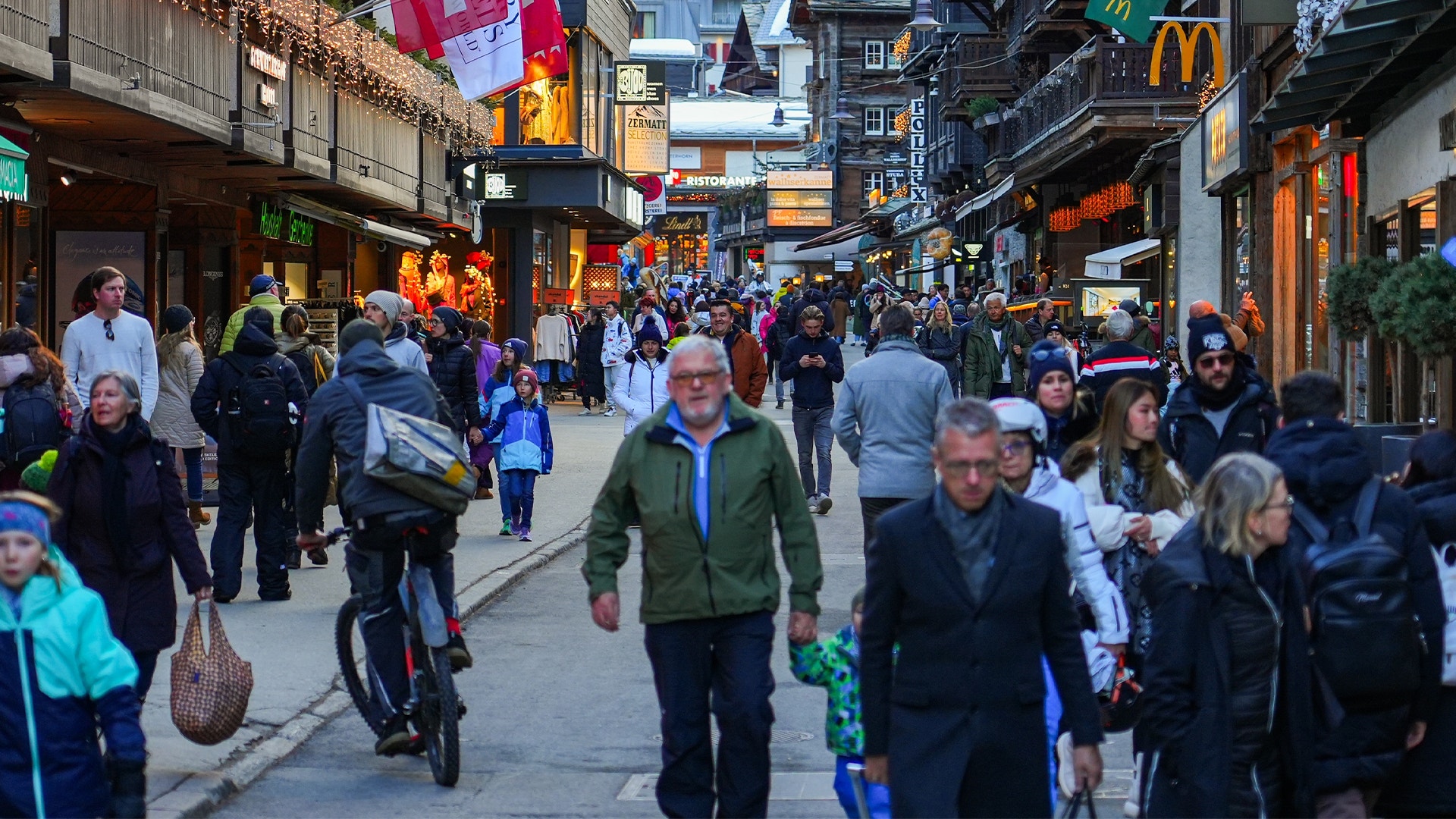 En fullsatt shoppinggata med många människor som handlar. Gatan är dekorerad med julpynt och omgiven av butiker med lysta skyltar.