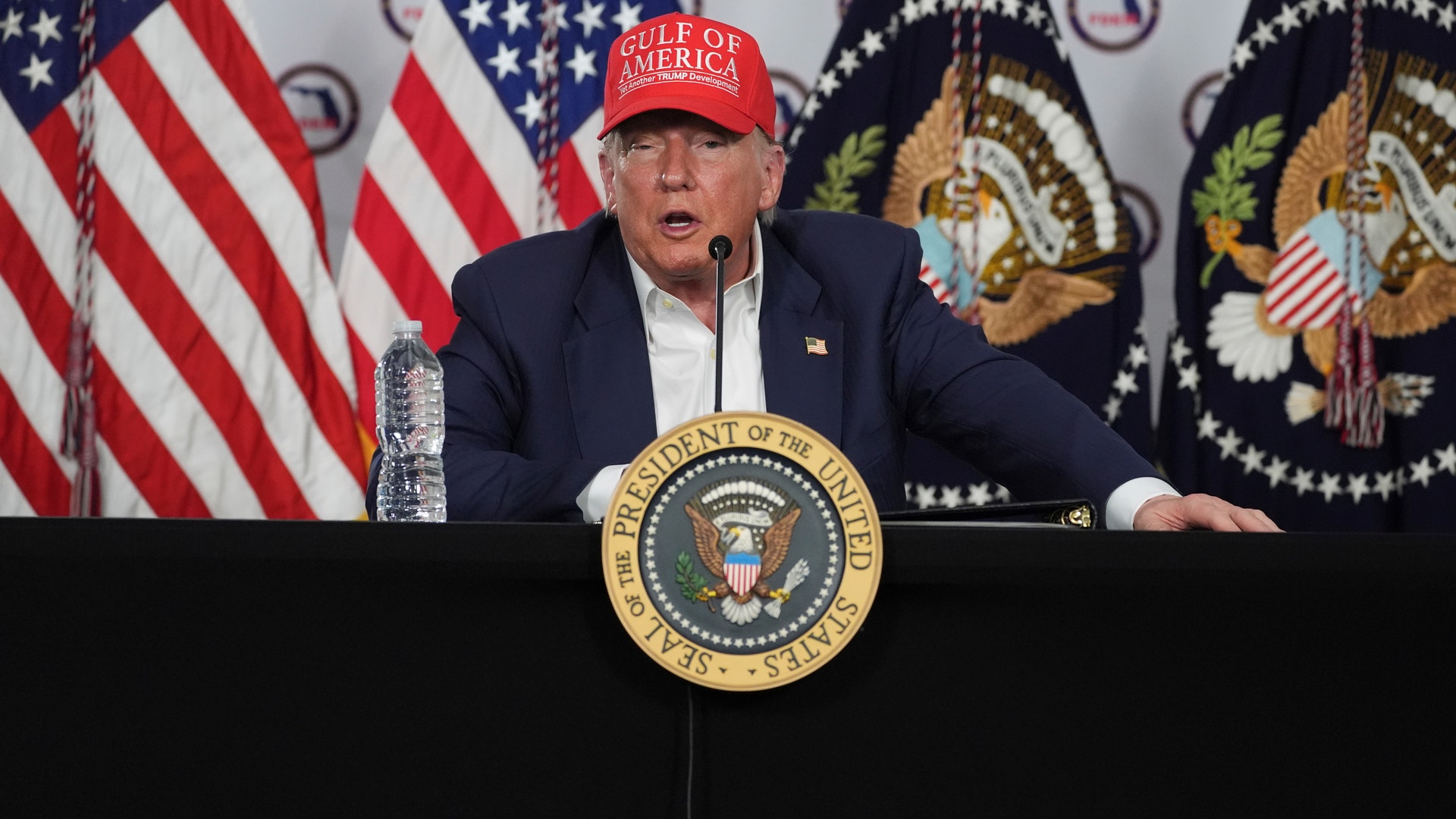 Donald Trump sitter vid ett bord framför amerikanska flaggor iklädd en röd keps med texten "Gulf of America".