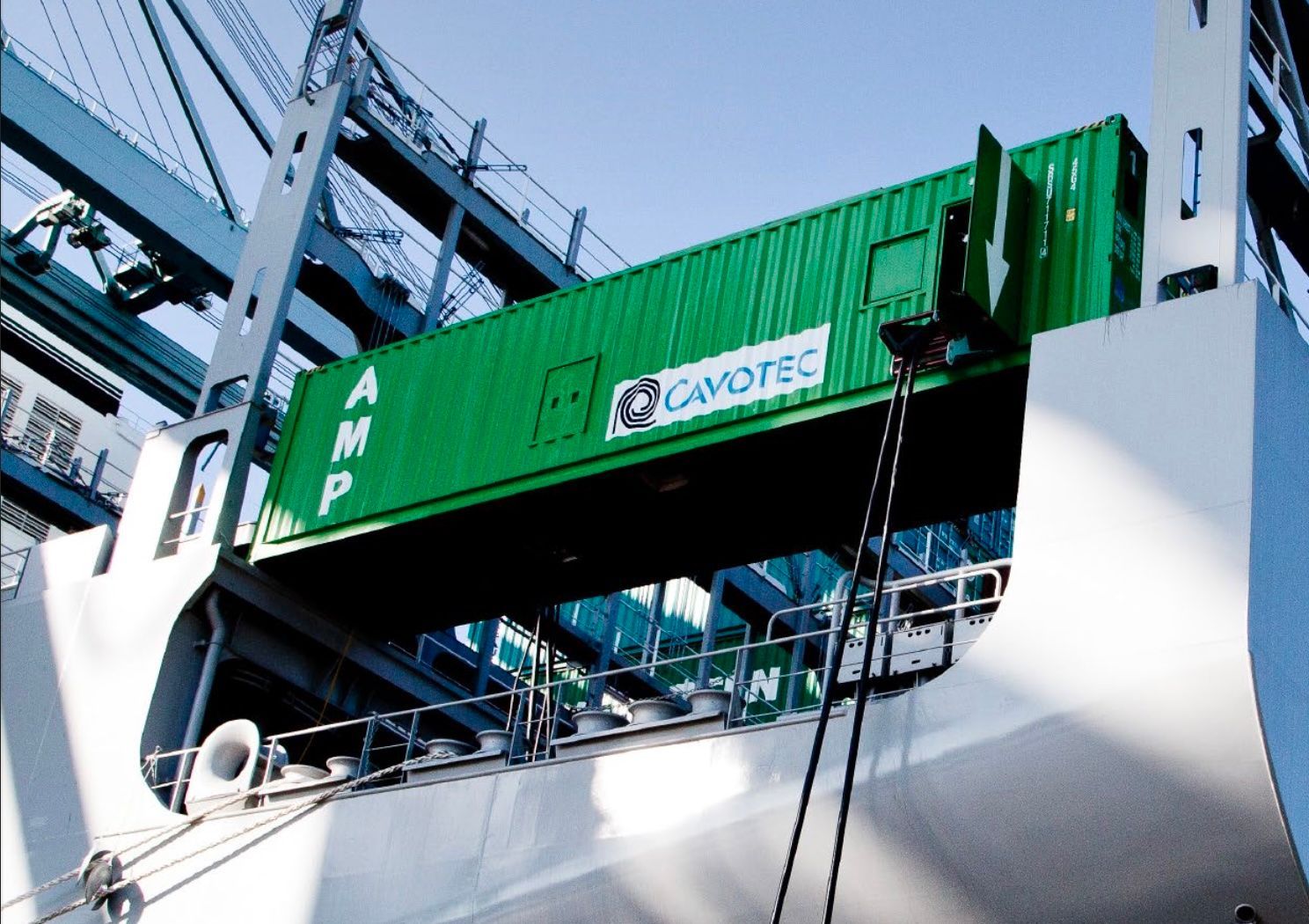 Ett fartyg i hamn med en grön Cavotec-container monterad på skrovet, med hamnkranar i bakgrunden.