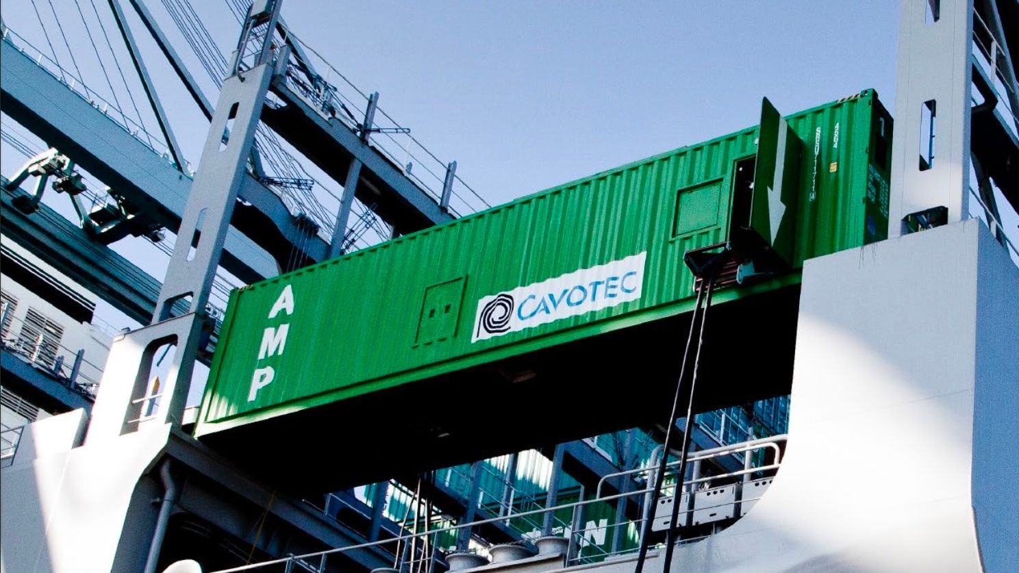 Ett fartyg i hamn med en grön Cavotec-container monterad på skrovet, med hamnkranar i bakgrunden.