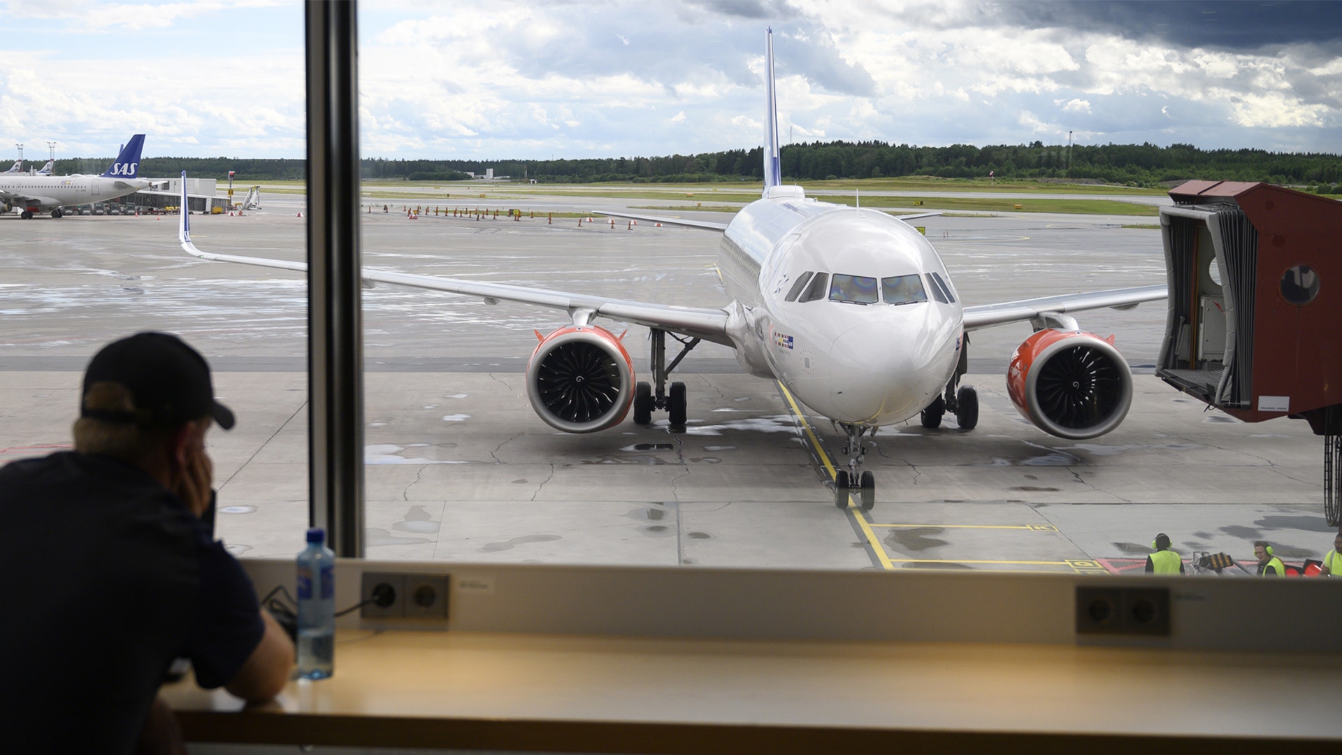 Passagerare tittar ut genom ett terminalfönster på ett parkerat flygplan vid gaten.