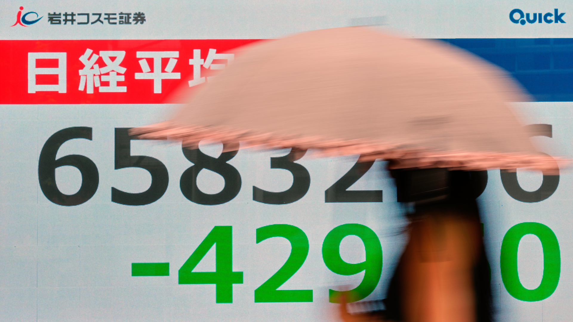 En hand pekar på en finansiell skärm som visar Nikkei 225-aktieindex med kursdata och röda och gröna siffror som anger prisförändringar.