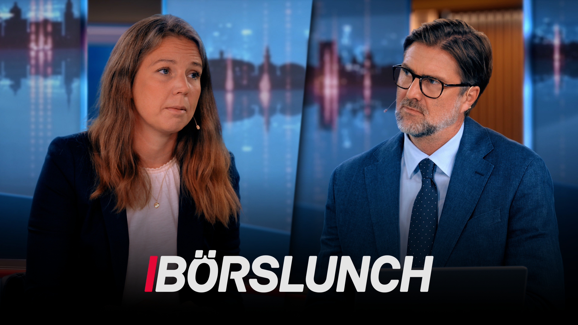 Två personer i en TV-studio för programmet Börslunch. En kvinna och en man sitter framför en bakgrund med en stadshorisont.