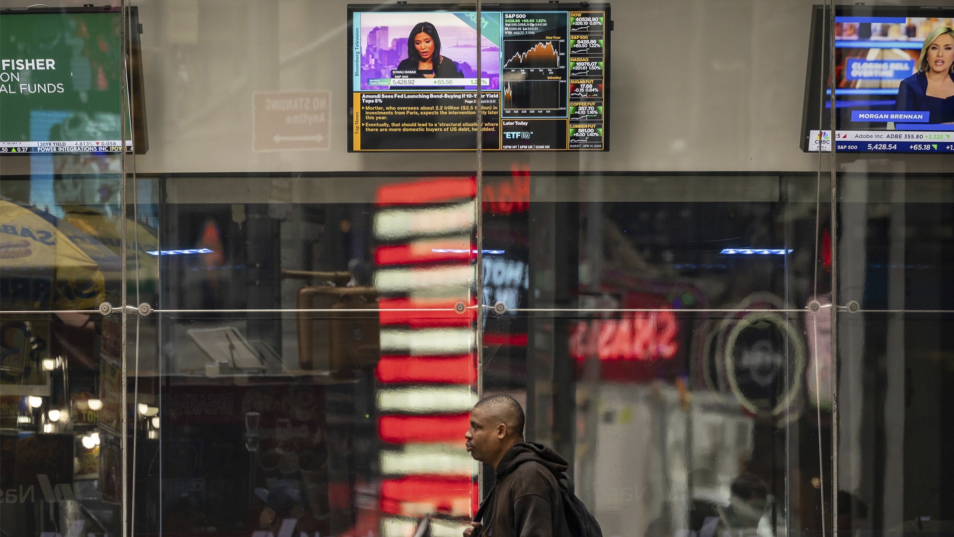 En man går förbi glasväggar på New York Stock Exchange med digitala börsticker och skärmar som visar aktiekurser i bakgrunden.