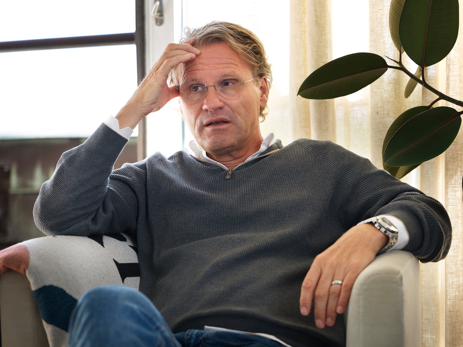 En man sitter i en soffa och pratar, med handen vid huvudet.