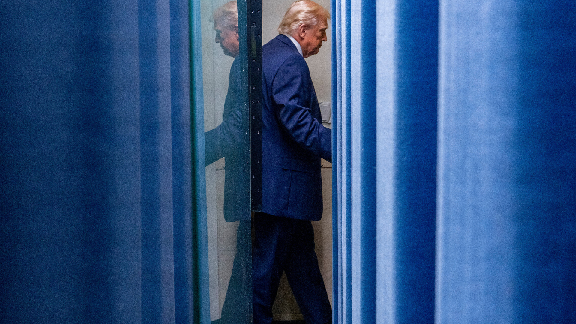 USA:s president Donald Trump går bakom ett blått skynke. 