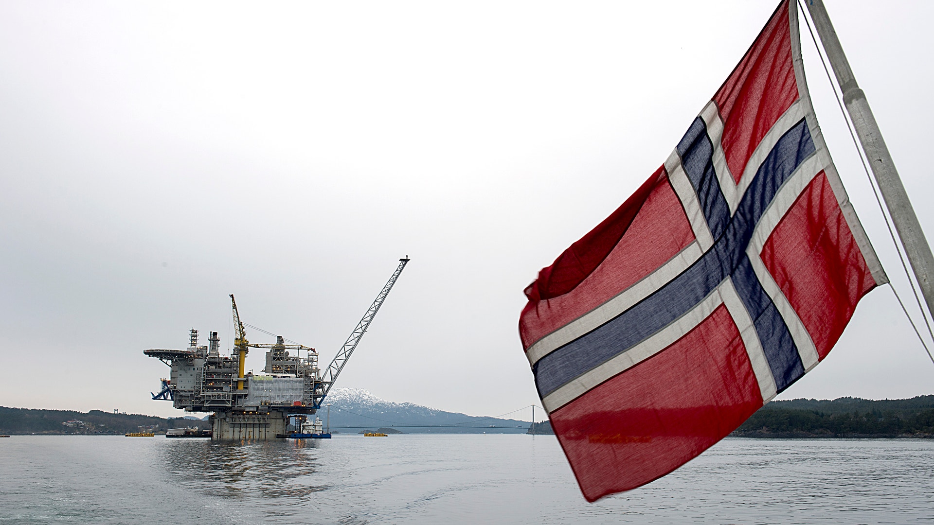 Norsk flagga på havet med en oljeplattform i bakgrunden