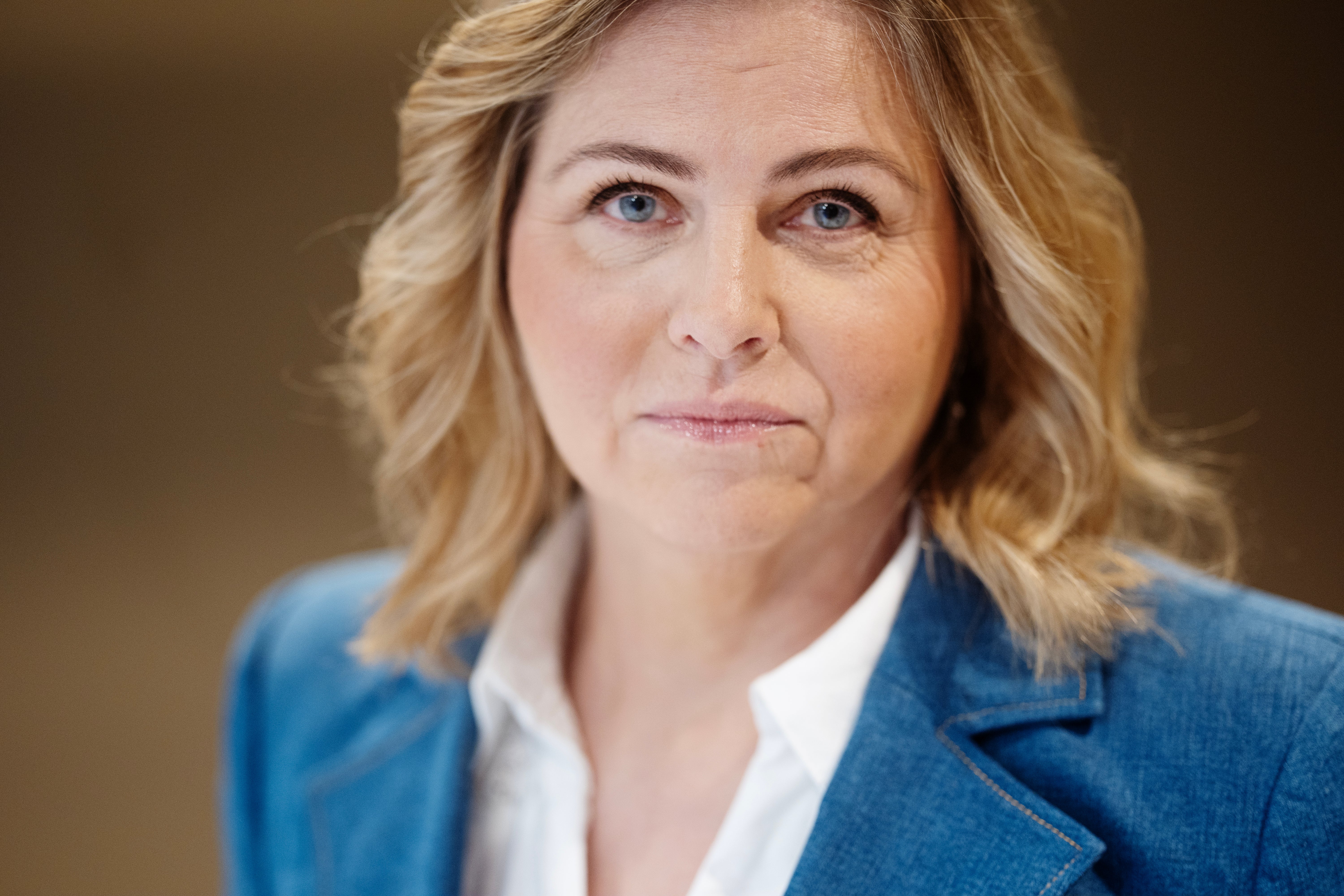 Porträtt av en kvinna med ljust vågigt hår och blå ögon, klädd i blå kavaj och vit skjorta.