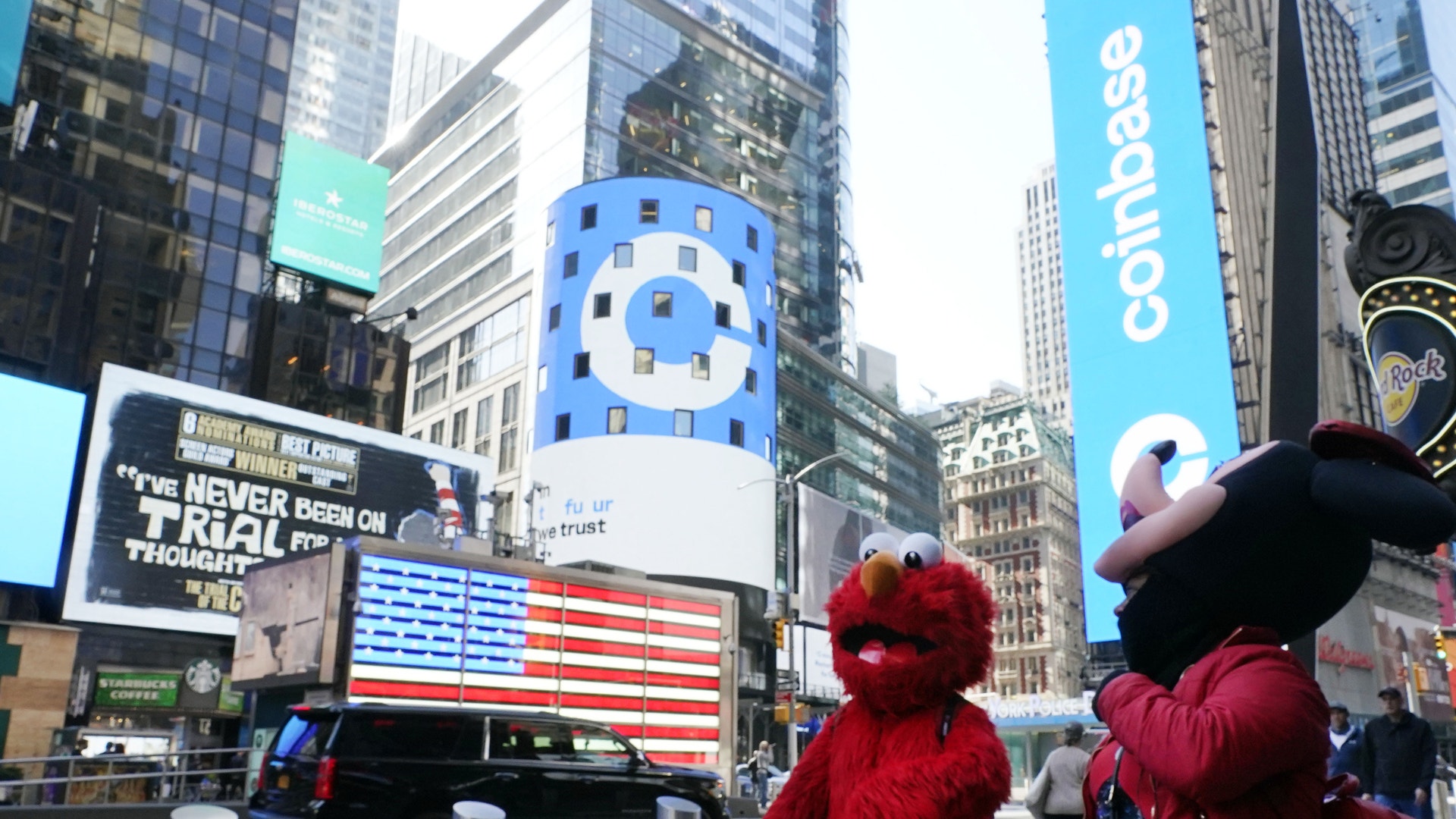 En livlig stadsmiljö med höga byggnader och digitala reklamskärmar, där två personer i röda kläder står i förgrunden.