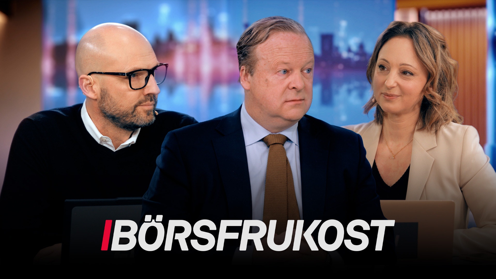 Tre personer i en TV-studio framför en blå stadshorisont. Text överst visar "BÖRSFRUKOST".
