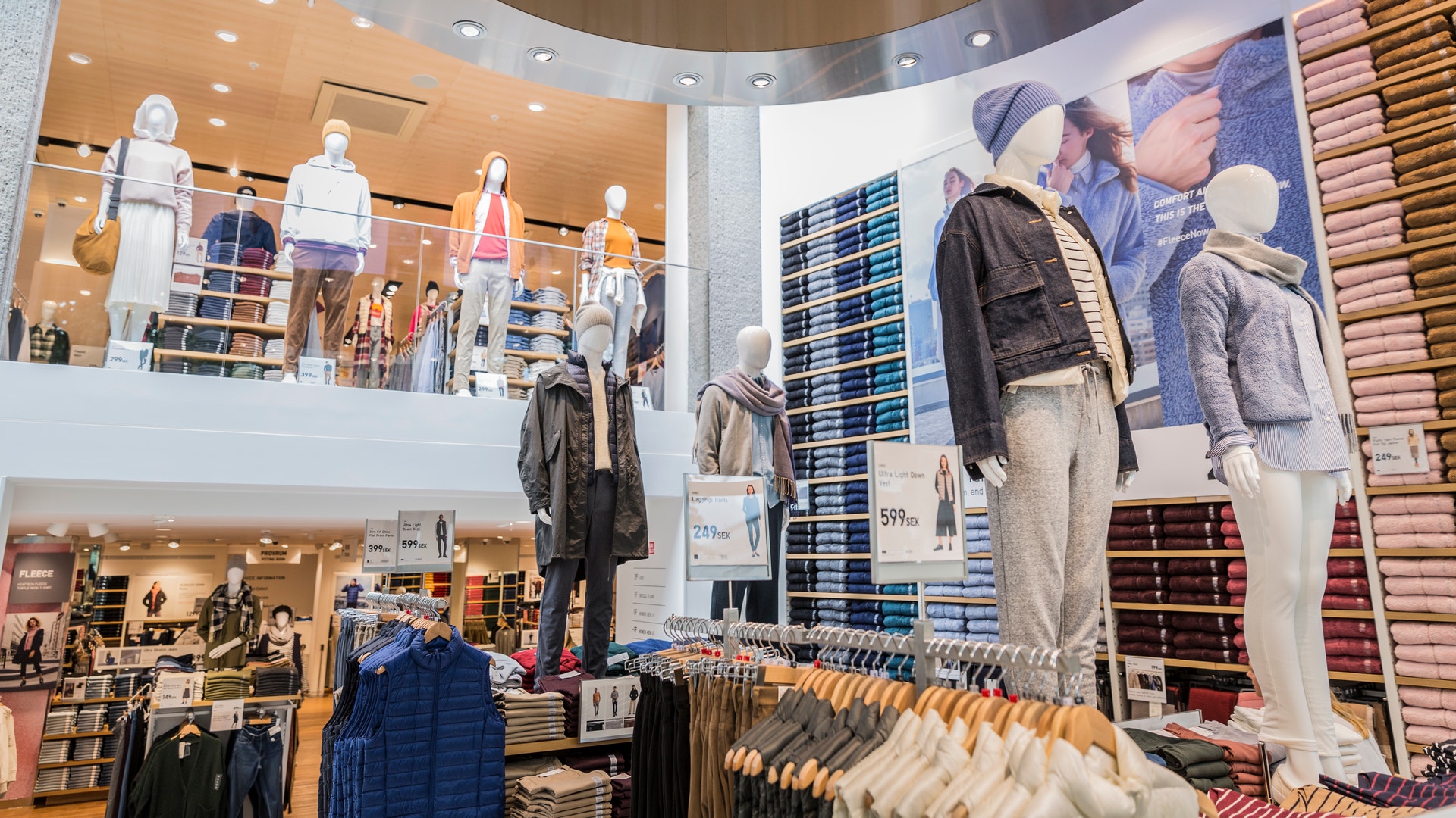 Interiör av en modern klädbutik med mannekänger, hängande plagg och hyllor med textilier på flera våningar.