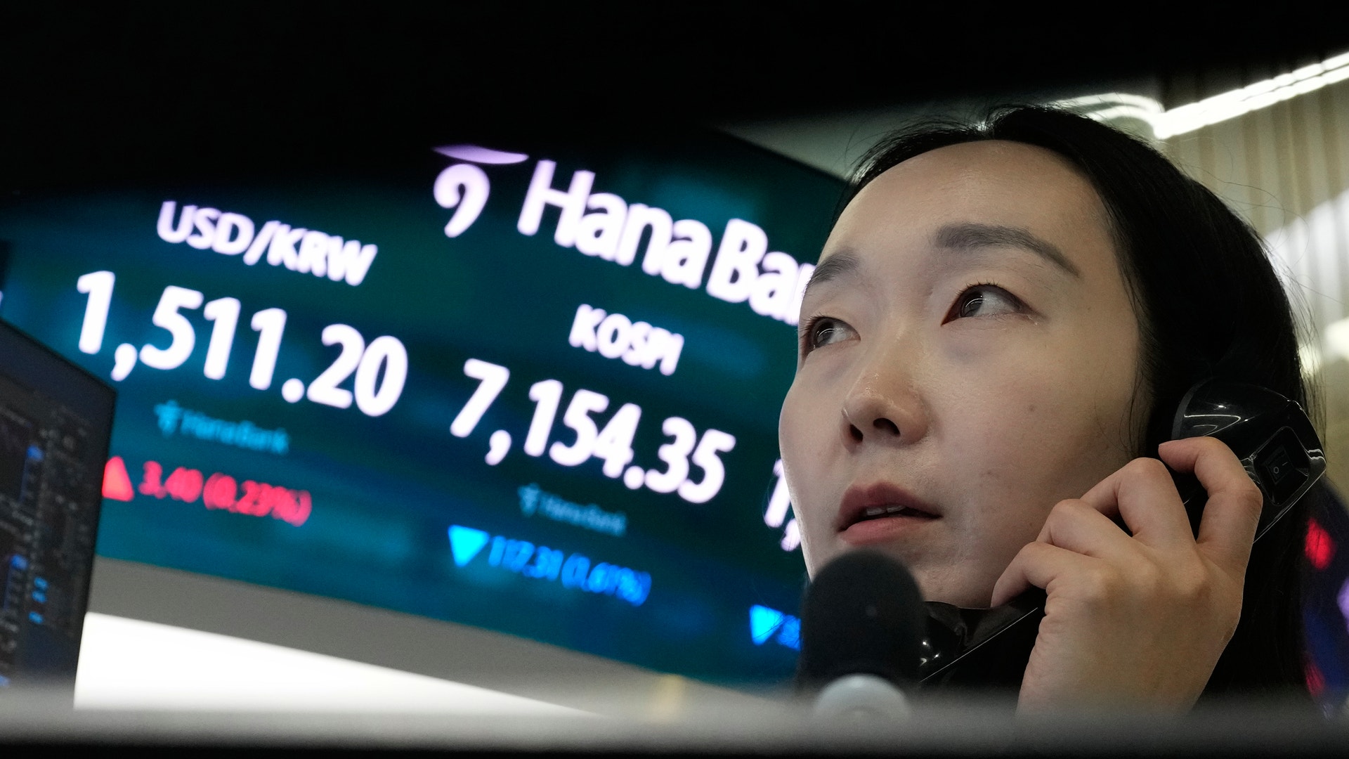Person som talar i telefon framför en skärm med valutakurser och finansiell data.