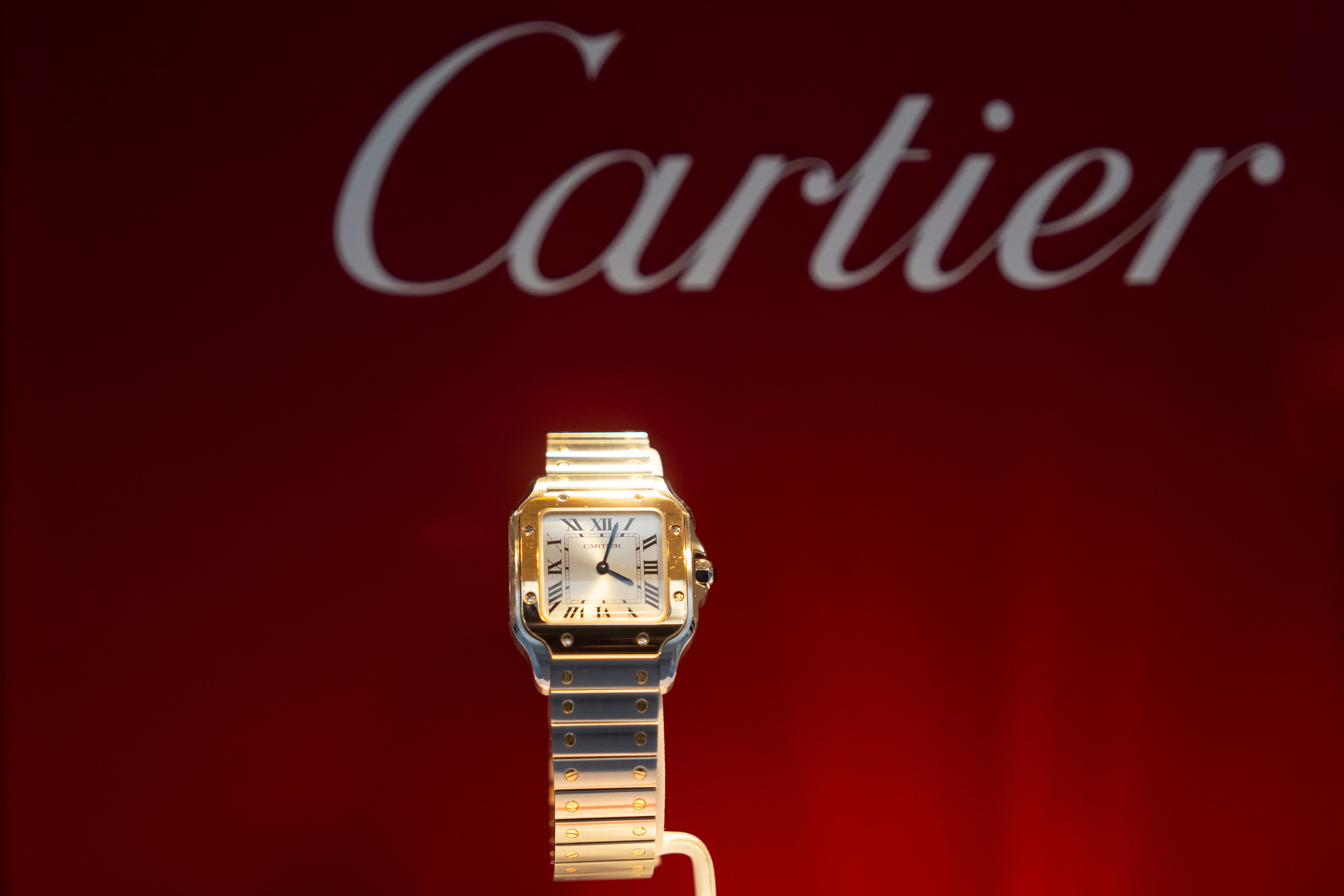 Cartier-klocka med kvadratiskt urtavla och två-färgat armband i guld och silver mot röd bakgrund.