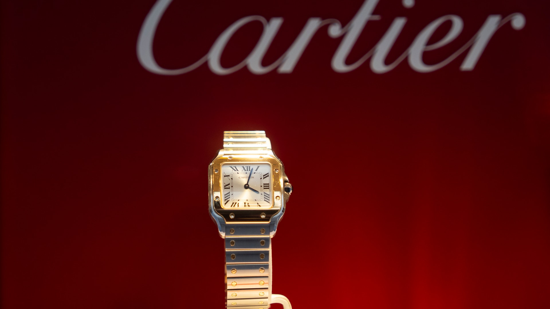 Cartier-klocka med kvadratiskt urtavla och två-färgat armband i guld och silver mot röd bakgrund.