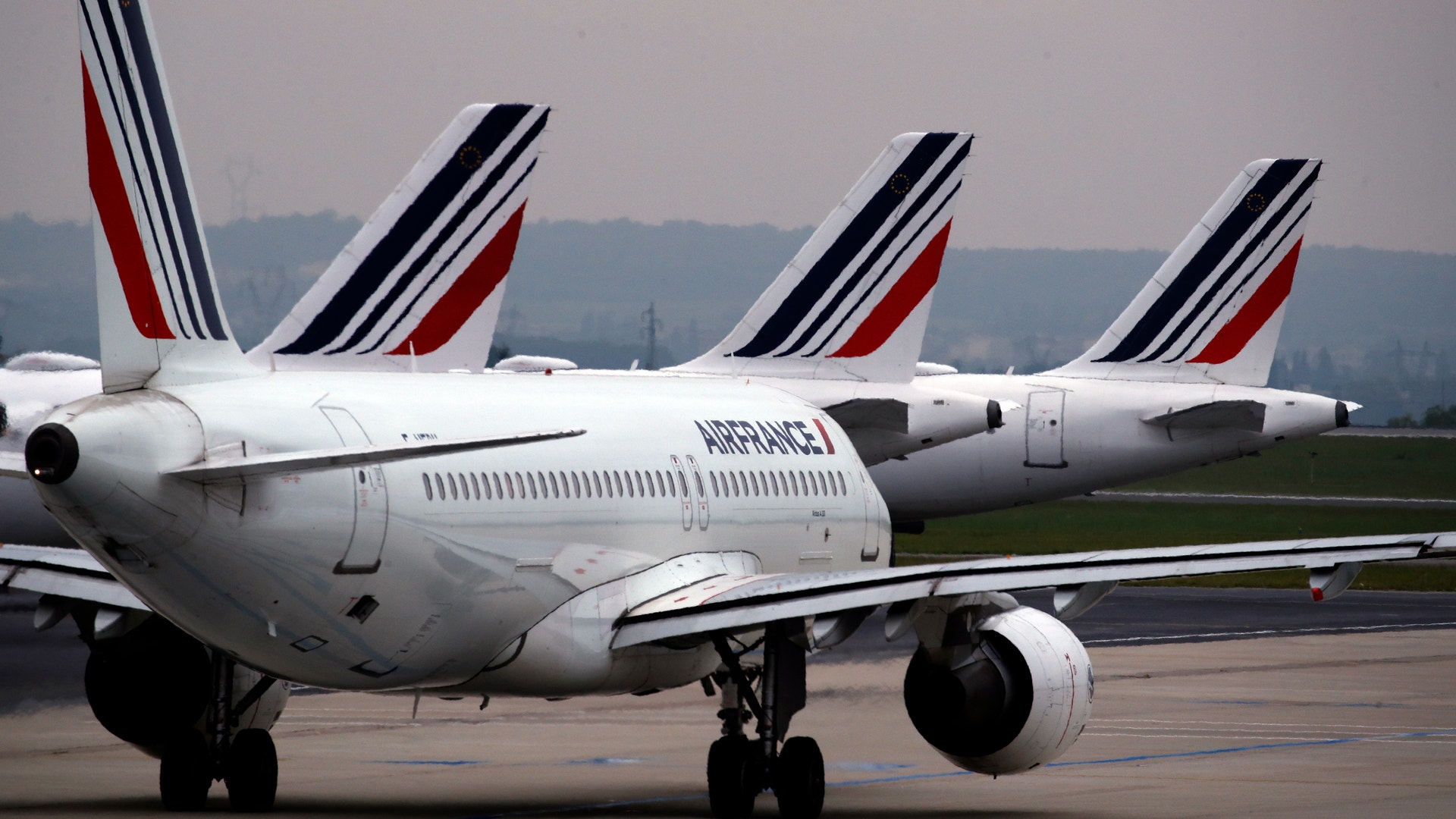 Vita Air France-flygplan parkerade på en landningsbana. Flera plan syns i rad med sina karakteristiska röd-blå-vita stjärtfenor.