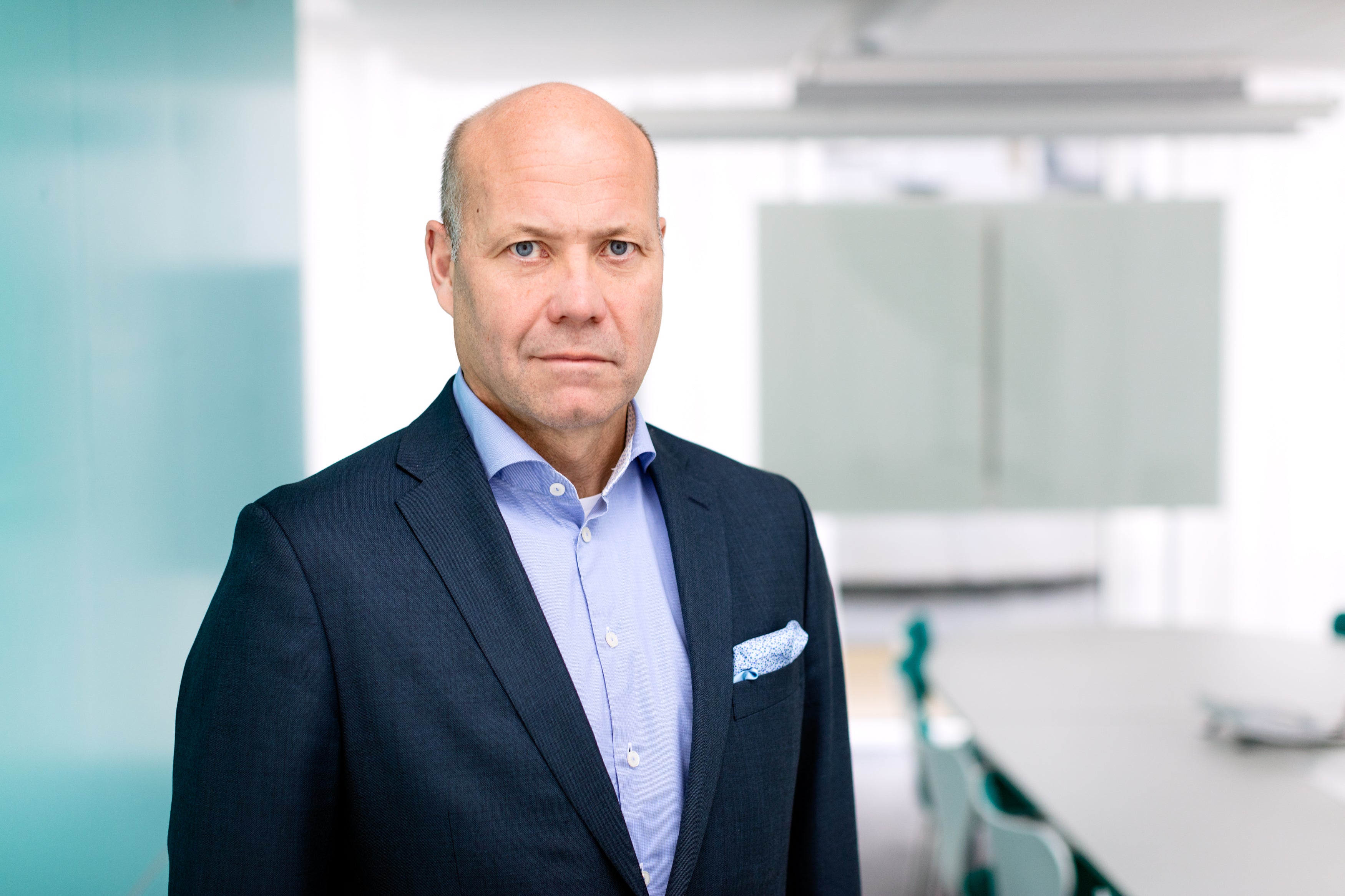 Porträtt av man i mörkblå kostym och ljusblå skjorta i en modern kontorsmiljö.