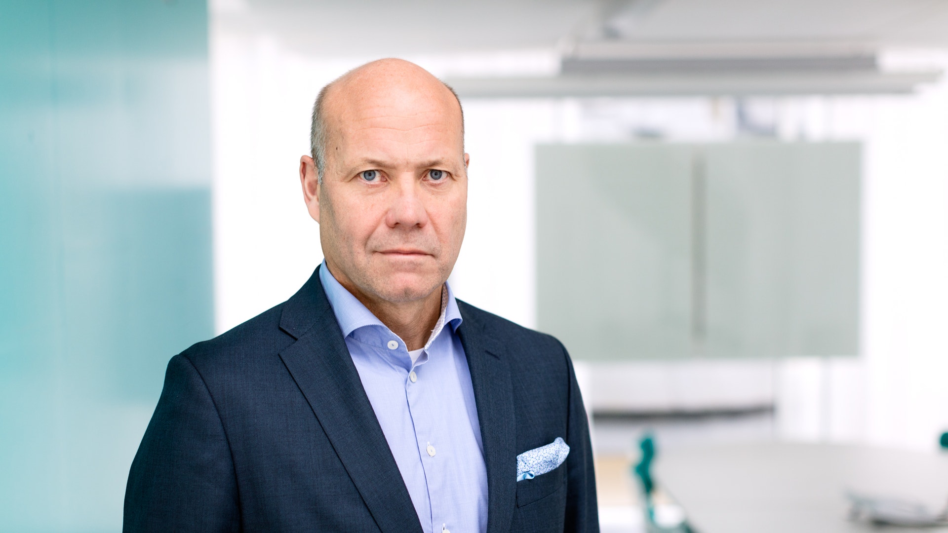 Porträtt av man i mörkblå kostym och ljusblå skjorta i en modern kontorsmiljö.