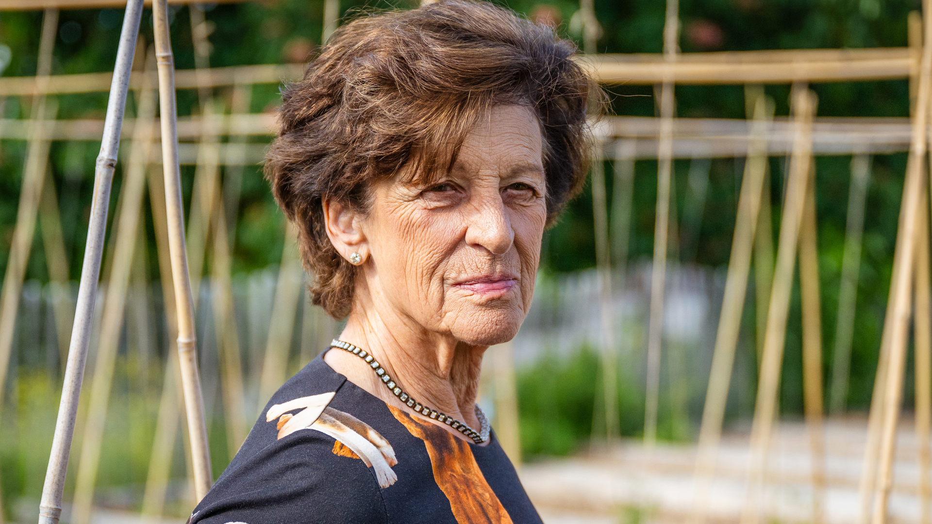 Porträtt av en äldre kvinna utomhus i en trädgård.