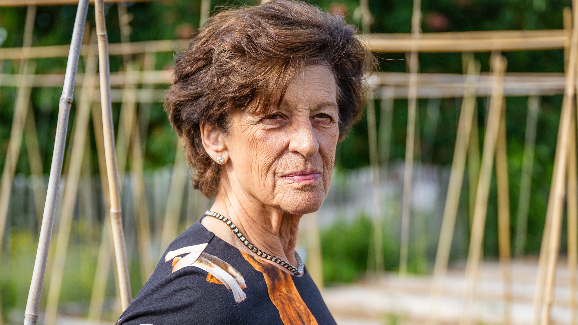 Porträtt av en äldre kvinna utomhus i en trädgård.