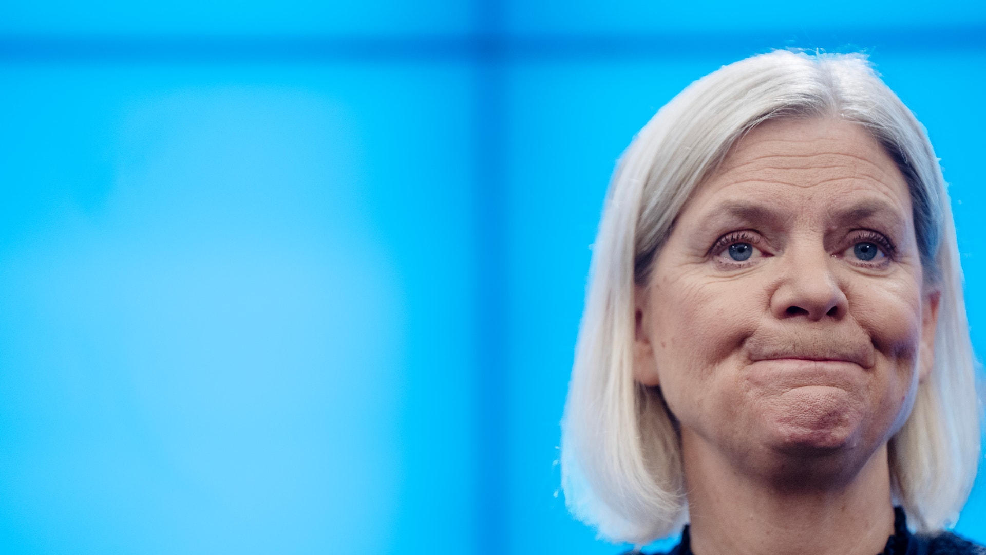 Porträtt av Magdalena Andersson med allvarlig min framför en blå bakgrund.