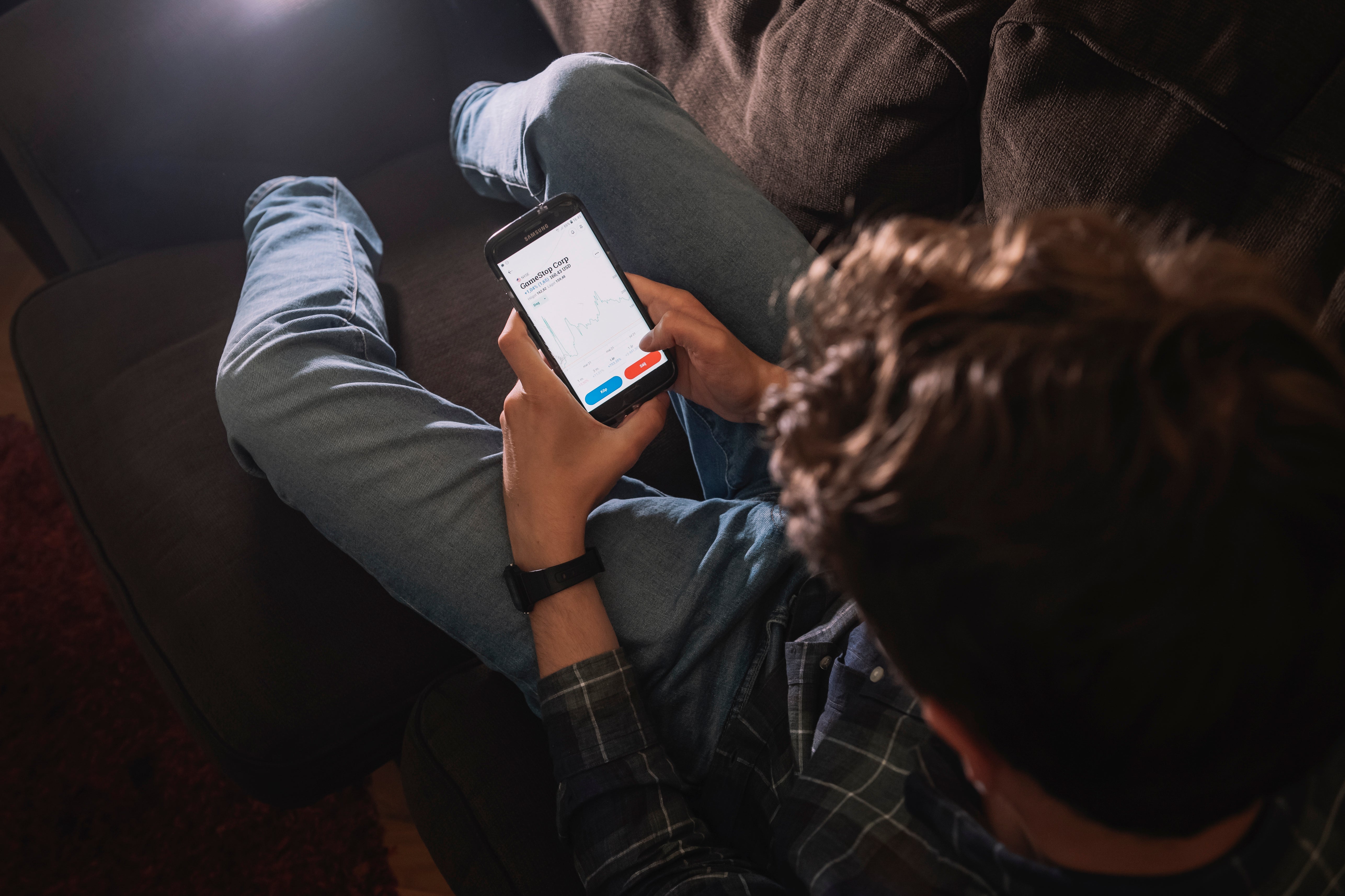 En person håller en smartphone i händerna och tittar på skärmen. Fotograferad uppifrån i svagt ljus.