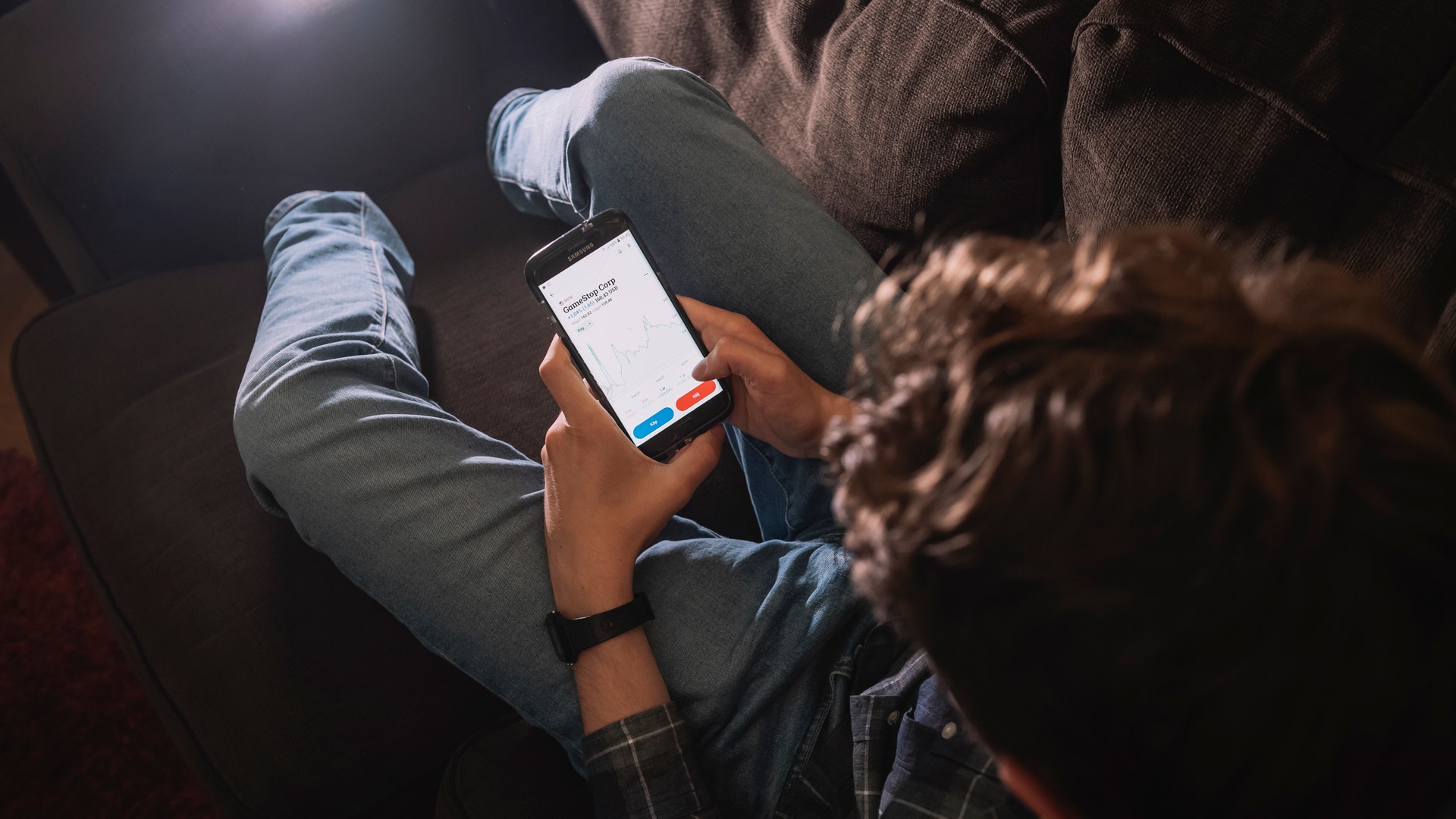 En person håller en smartphone i händerna och tittar på skärmen. Fotograferad uppifrån i svagt ljus.