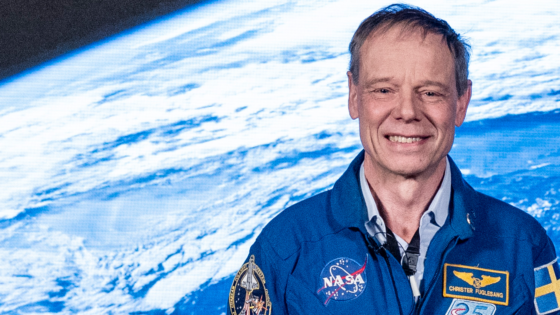 Porträtt av astronaut i blå NASA-rymddräkt med jorden synlig i bakgrunden från rymden.