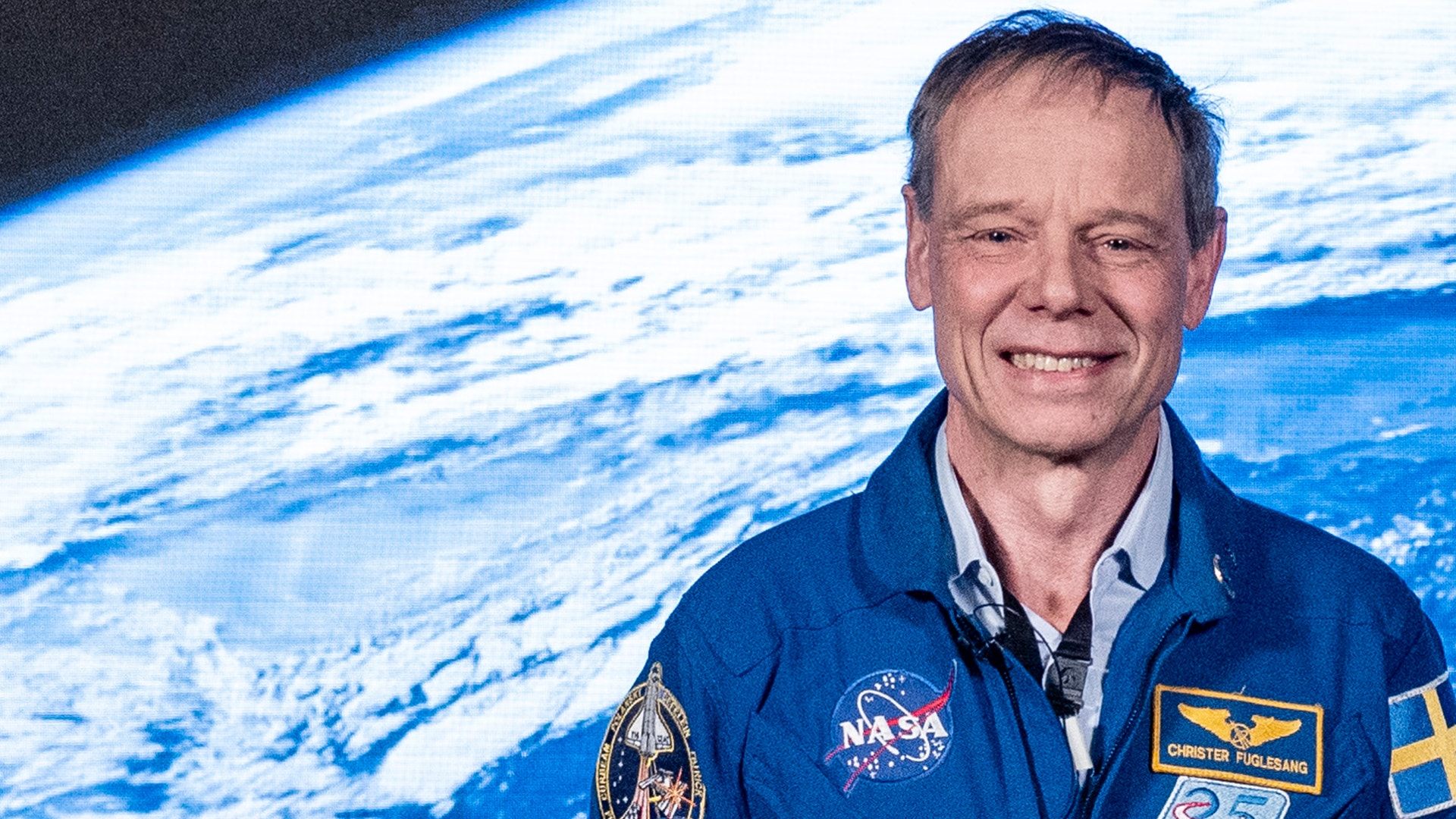 Porträtt av astronaut i blå NASA-rymddräkt med jorden synlig i bakgrunden från rymden.