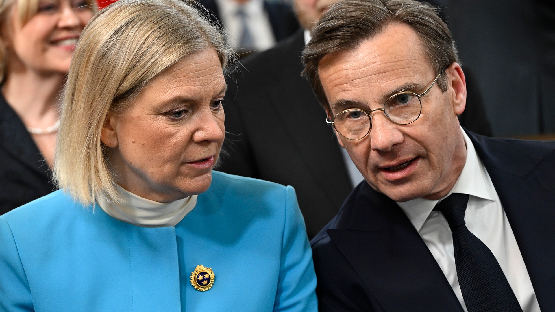 En kvinna och en man i samtal, sittande bredvid varandra i en sal.