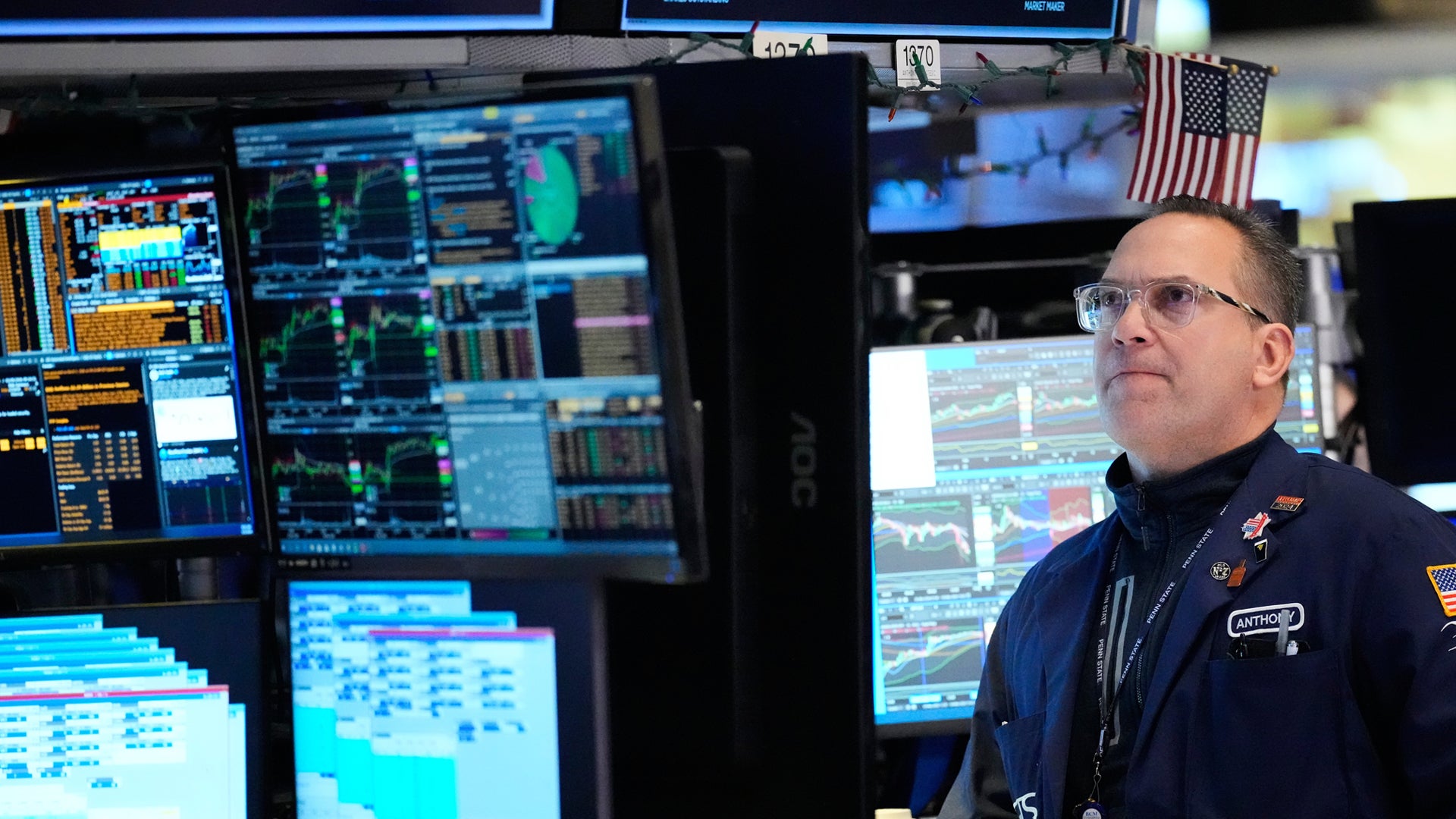 En person i blå uniform arbetar vid en kontrollpanel med flera datorskärmar som visar data och kartöversikter.